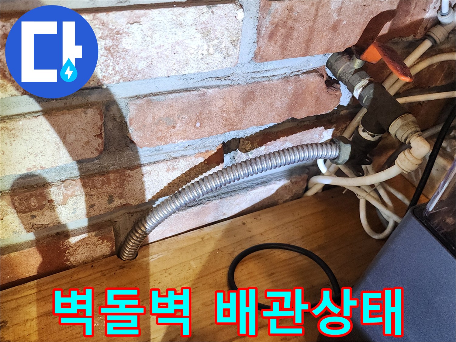 벽돌로 된 벽면 아래에 노출된 금속 재질의 주름관과 수도 밸브 연결 부위