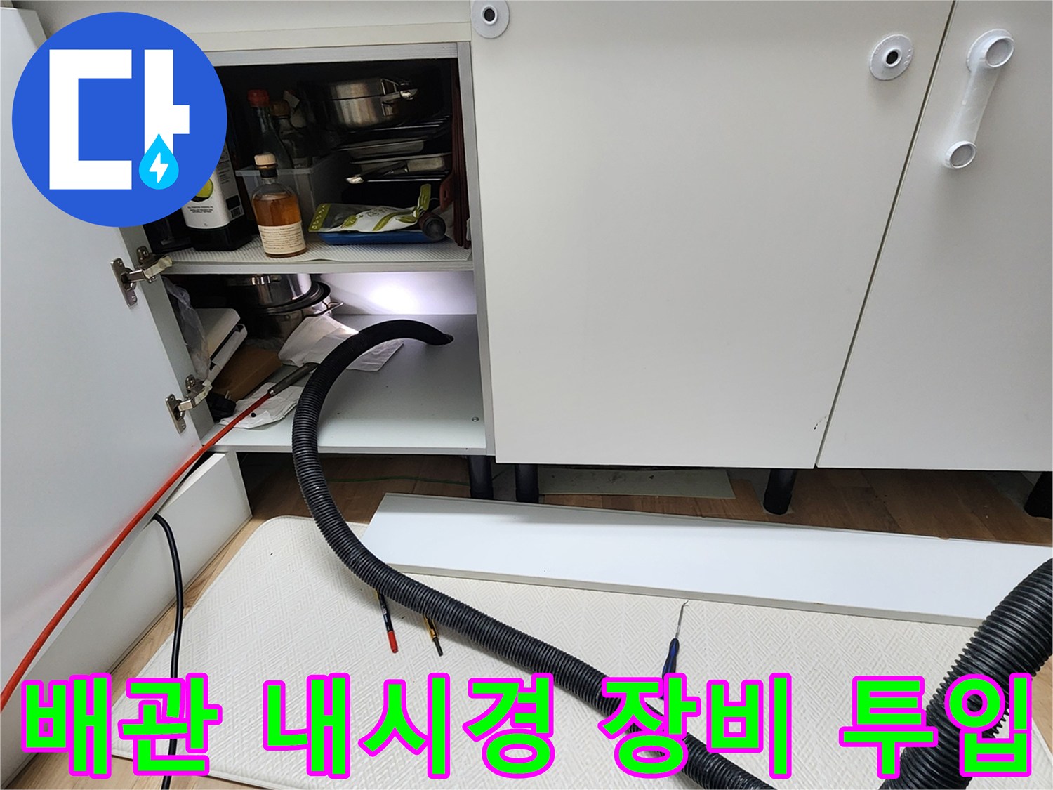 싱크대 하부장 배관 내부를 조사하기 위해 검은색 호스를 삽입한 장면입니다.