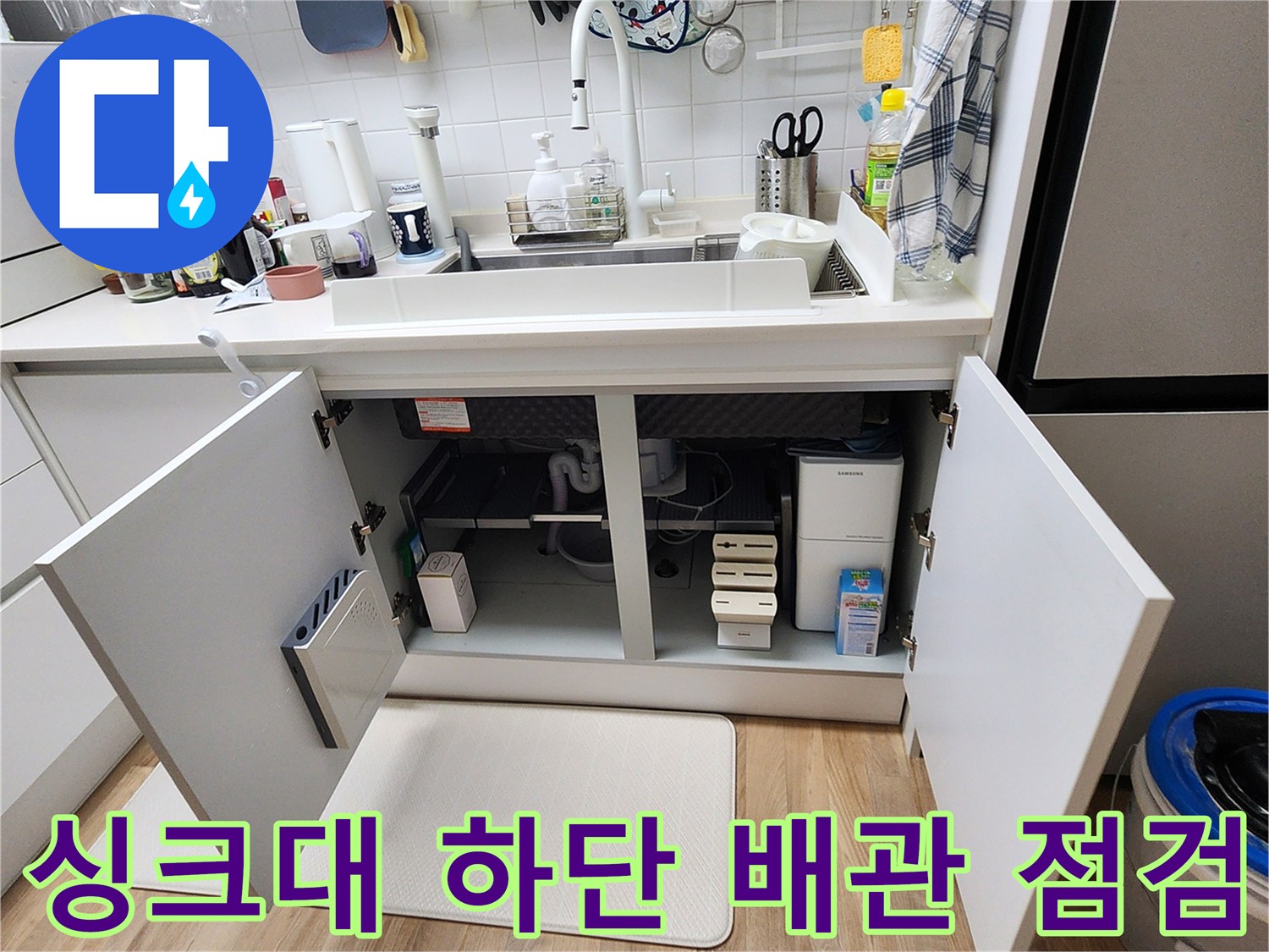 열려있는 싱크대 하부장 내부의 복잡한 배관과 분배기 모습