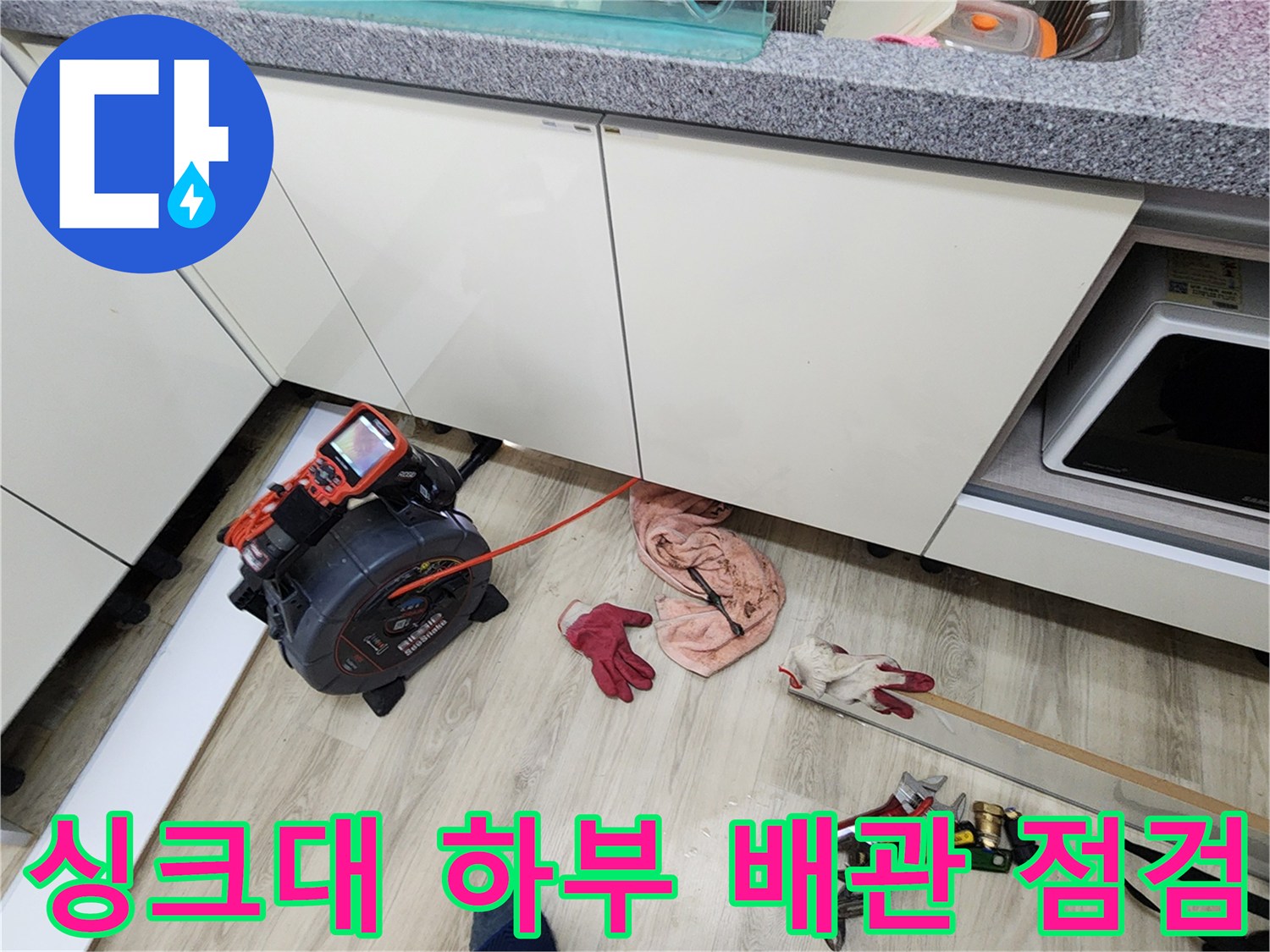 주방 싱크대 아래쪽 공간에서 배관 압력을 측정하는 장비와 도구가 놓여 있는 모습입니다.