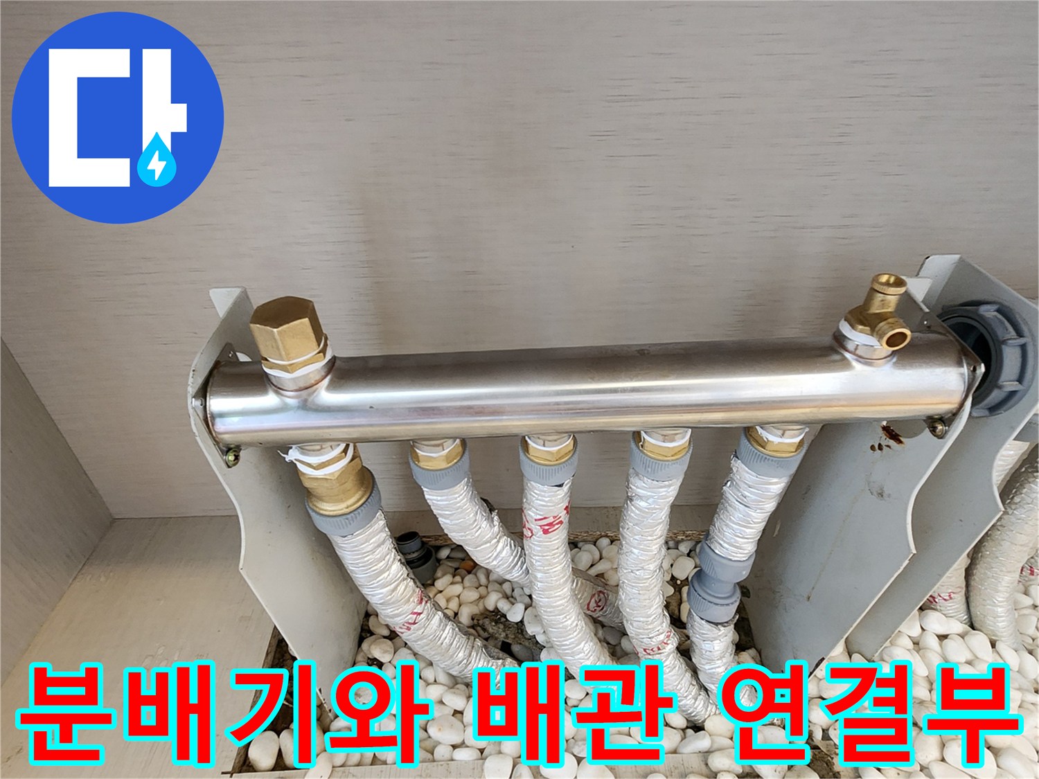 금속 재질의 분배기와 보온재로 감싸진 배관들이 자갈층 위에 배치된 모습