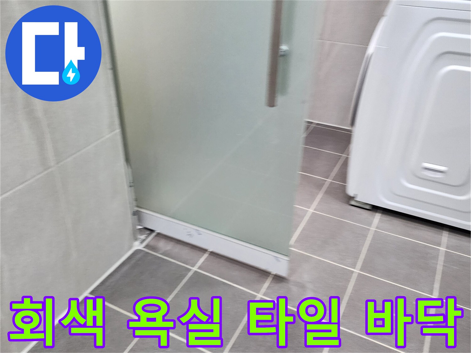 욕실 내부의 회색 타일과 세탁기 및 유리 파티션 하단 모습