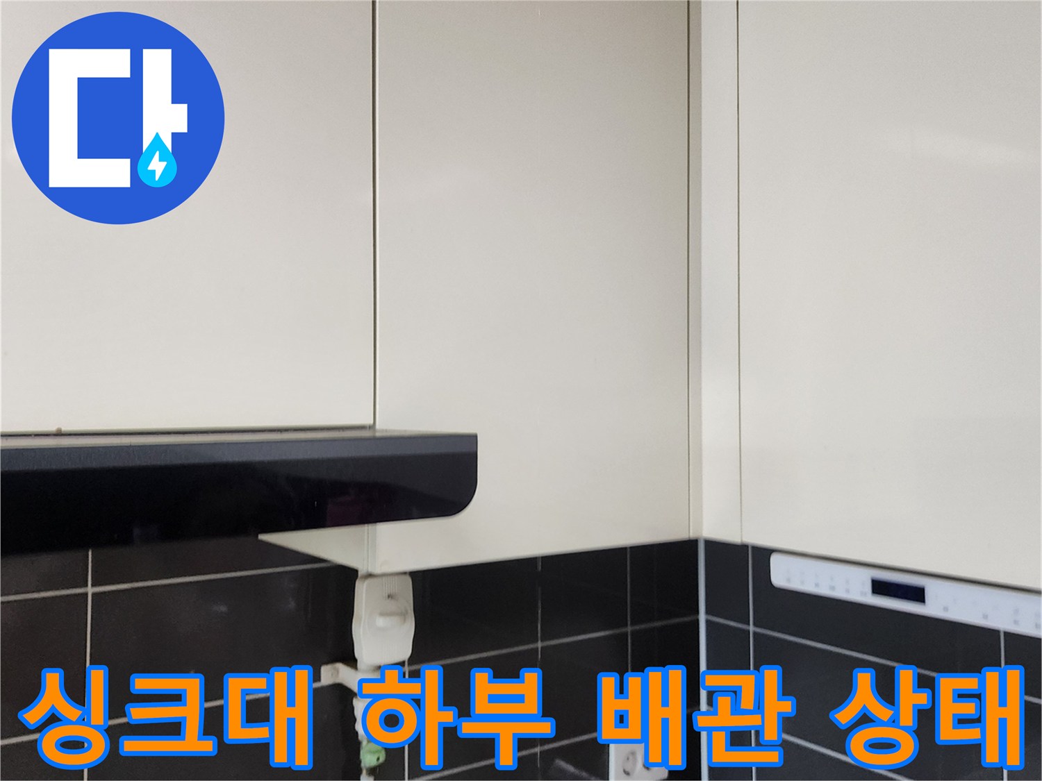 싱크대 밑 배관과 벽면 타일 및 콘센트의 모습