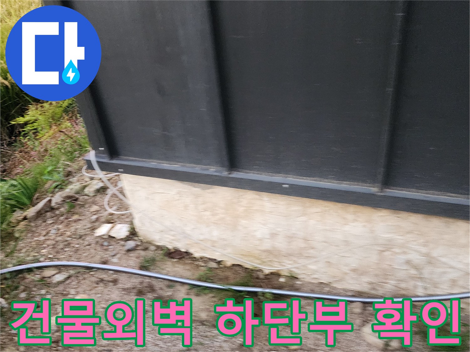 검은색 외벽 패널 아래로 보이는 콘크리트 기초 부분의 습기 상태를 촬영한 사진입니다.