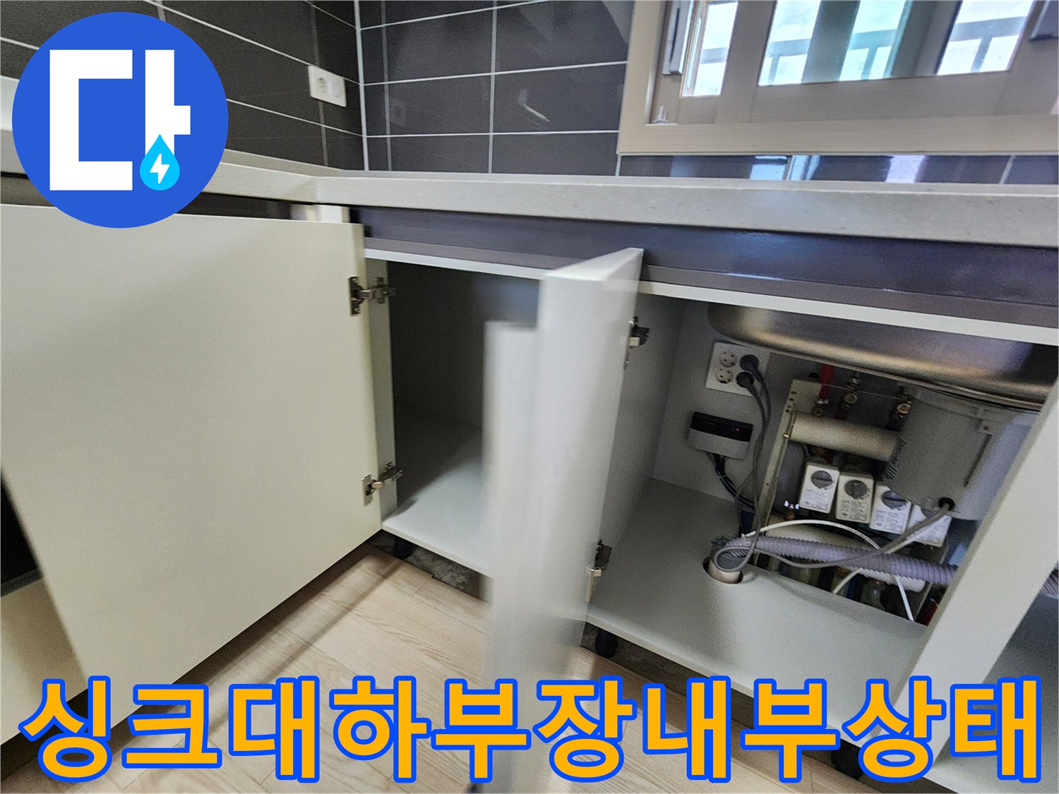 열린 싱크대 하부장-노출된 배관과 벽면 콘센트 확인
