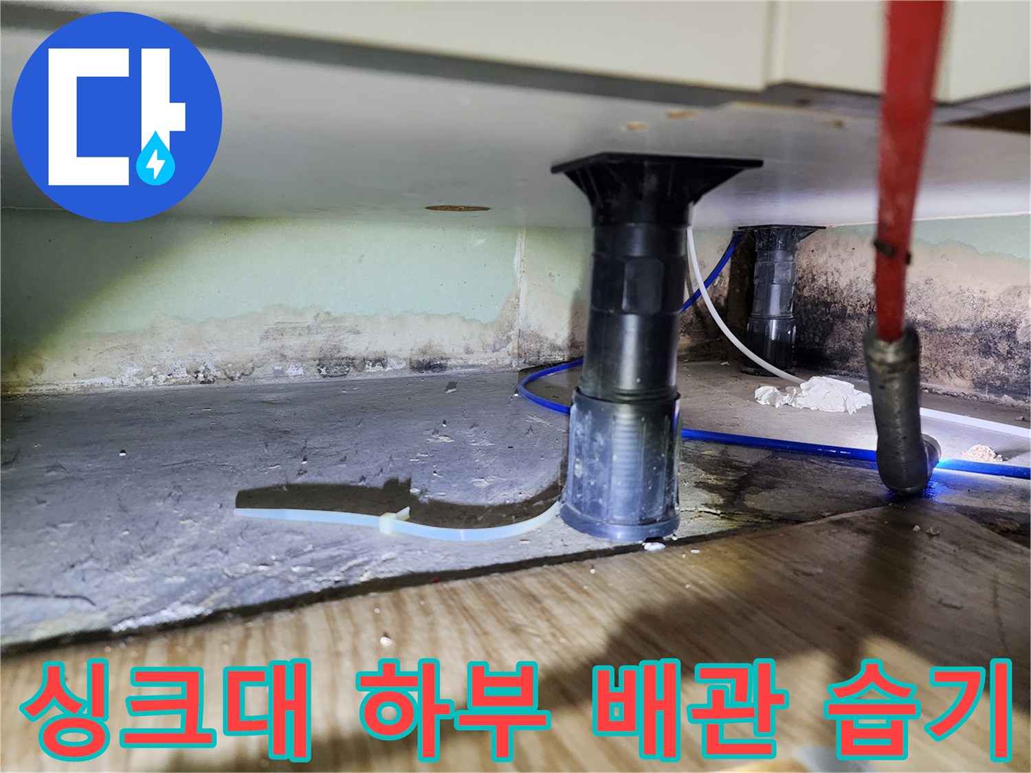 주방 싱크대 아래쪽 배관 주변의 젖은 바닥과 벽면 얼룩 상세 사진