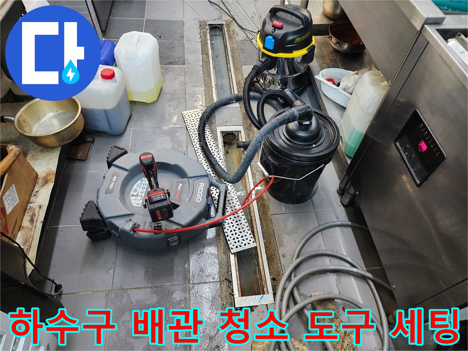 주방 바닥 트렌치 옆에 놓인 산업용 흡입기와 배관 청소 장비들