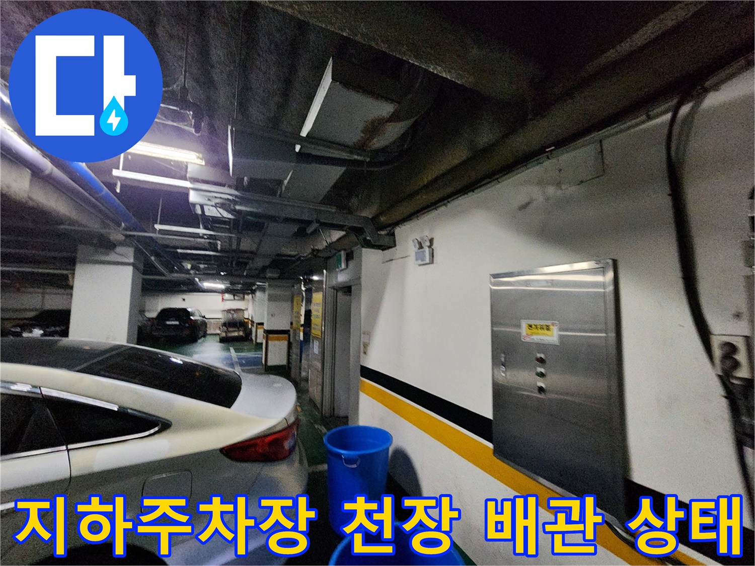 지하 주차장 천장 부근의 노출된 배관과 벽면 전기 분전함 모습