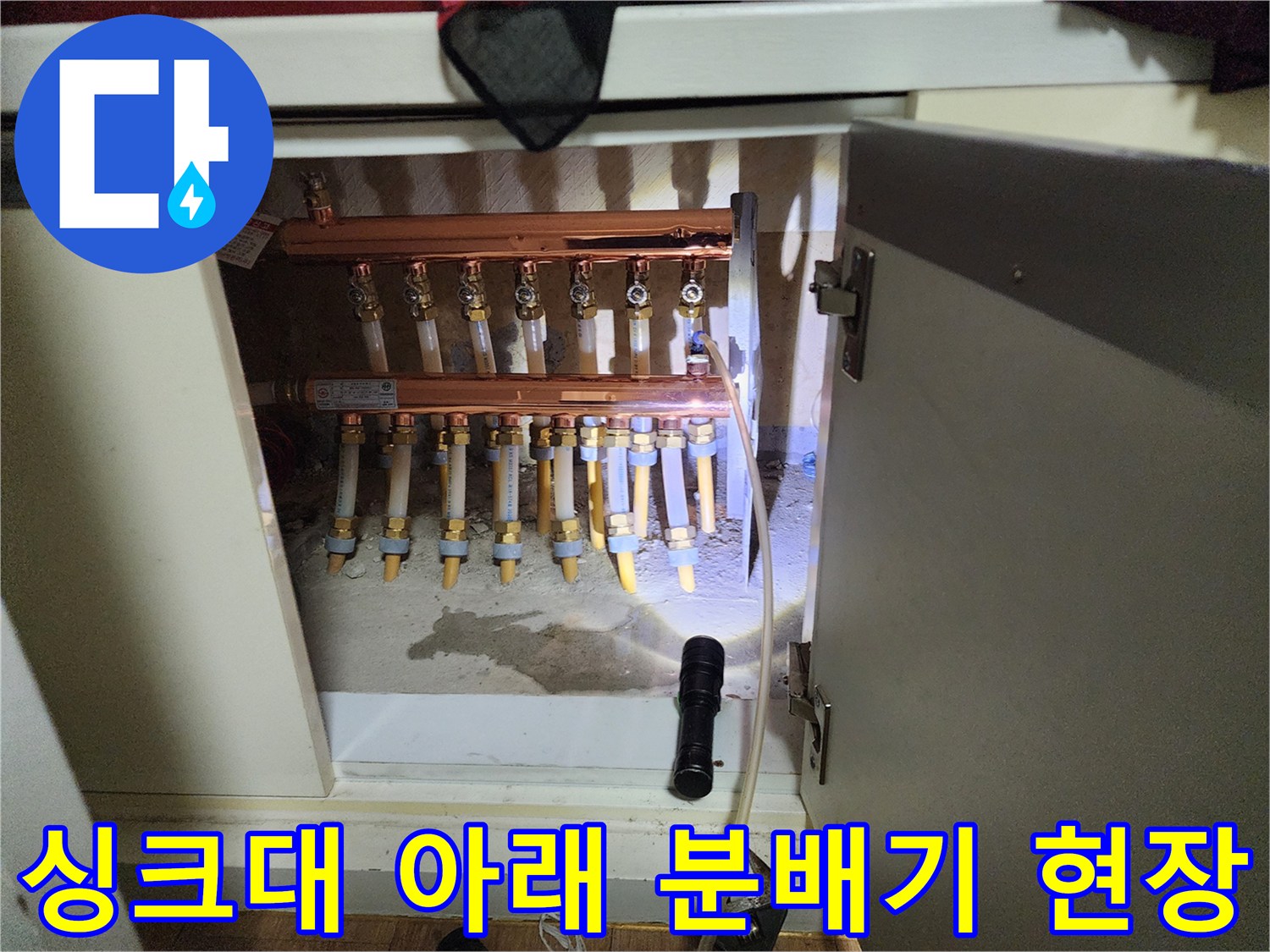 싱크대 하단 공간에 설치된 난방 분배기와 연결된 여러 개의 배관들입니다.