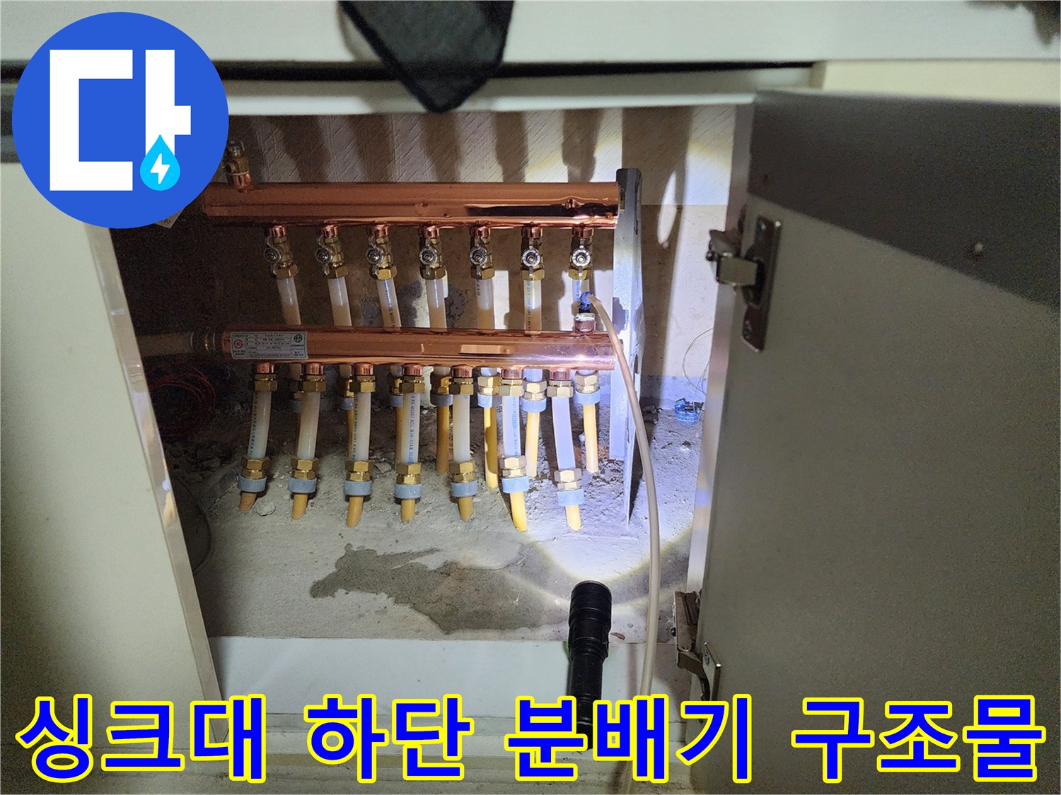 싱크대 하부장에 위치한 난방 배관 및 분배기 사진입니다.