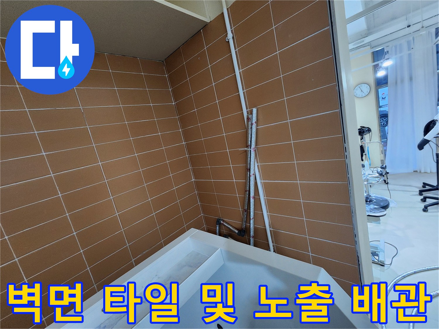 갈색 타일 벽에 설치된 수직 배관과 샴푸대 일부