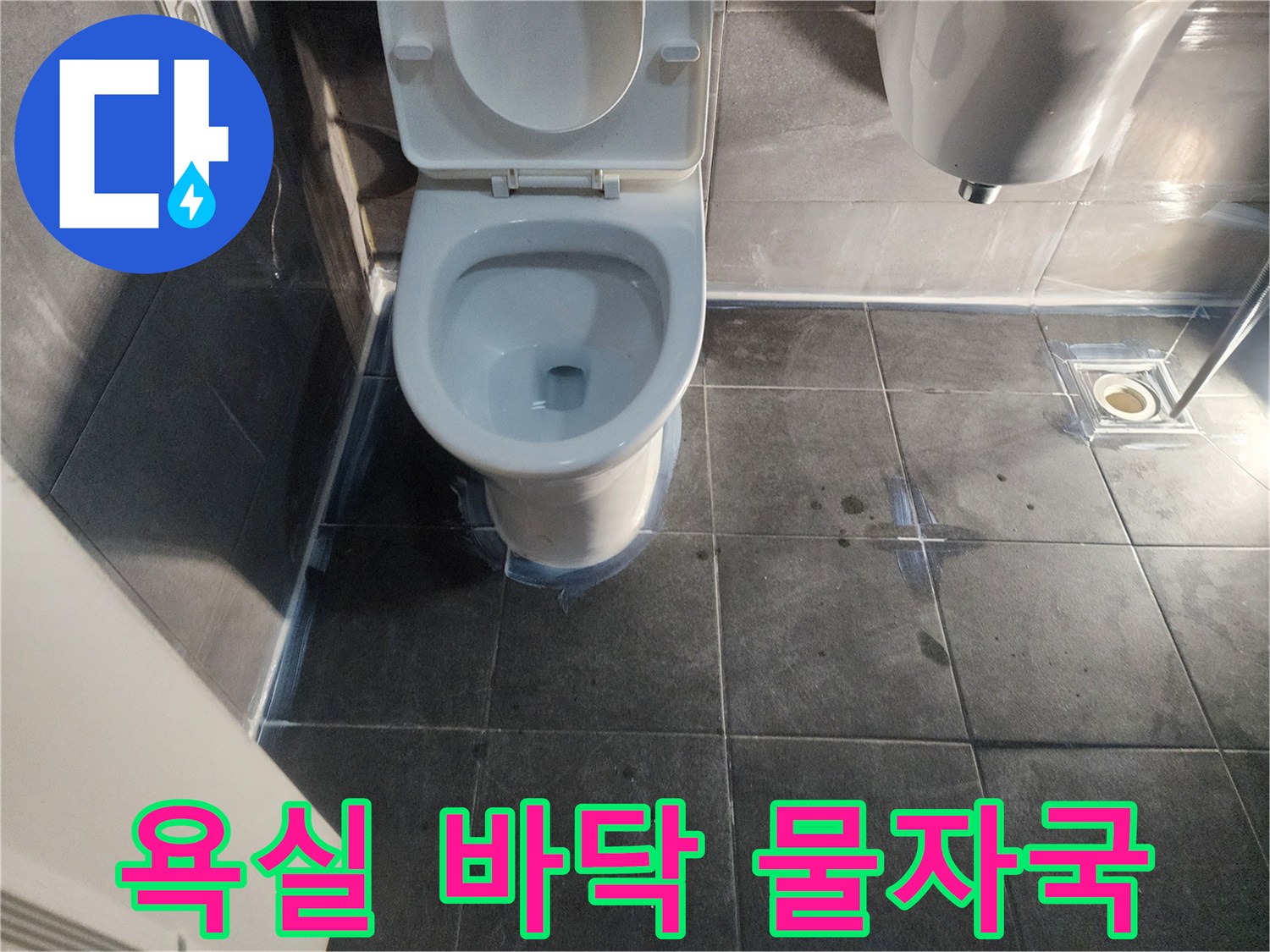 어두운 색상의 화장실 타일 위에 번져 있는 물자국과 습기