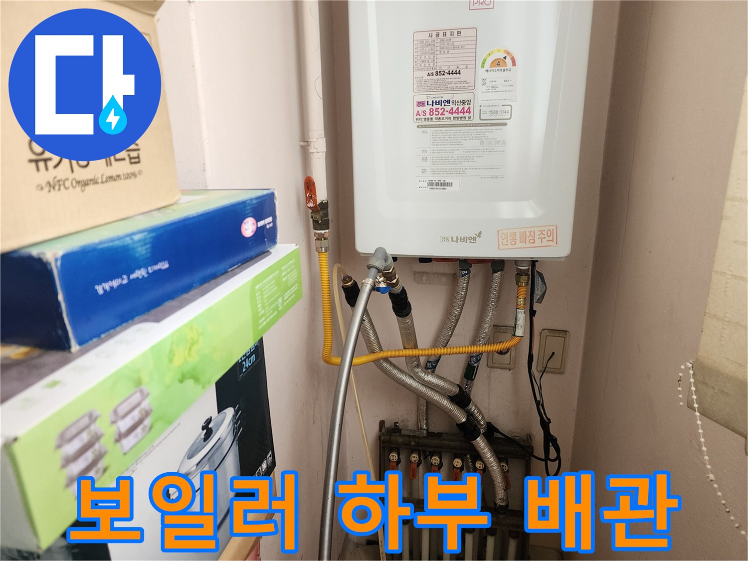 보일러 아래쪽으로 연결된 여러 개의 금속 및 플라스틱 배관 모습입니다.
