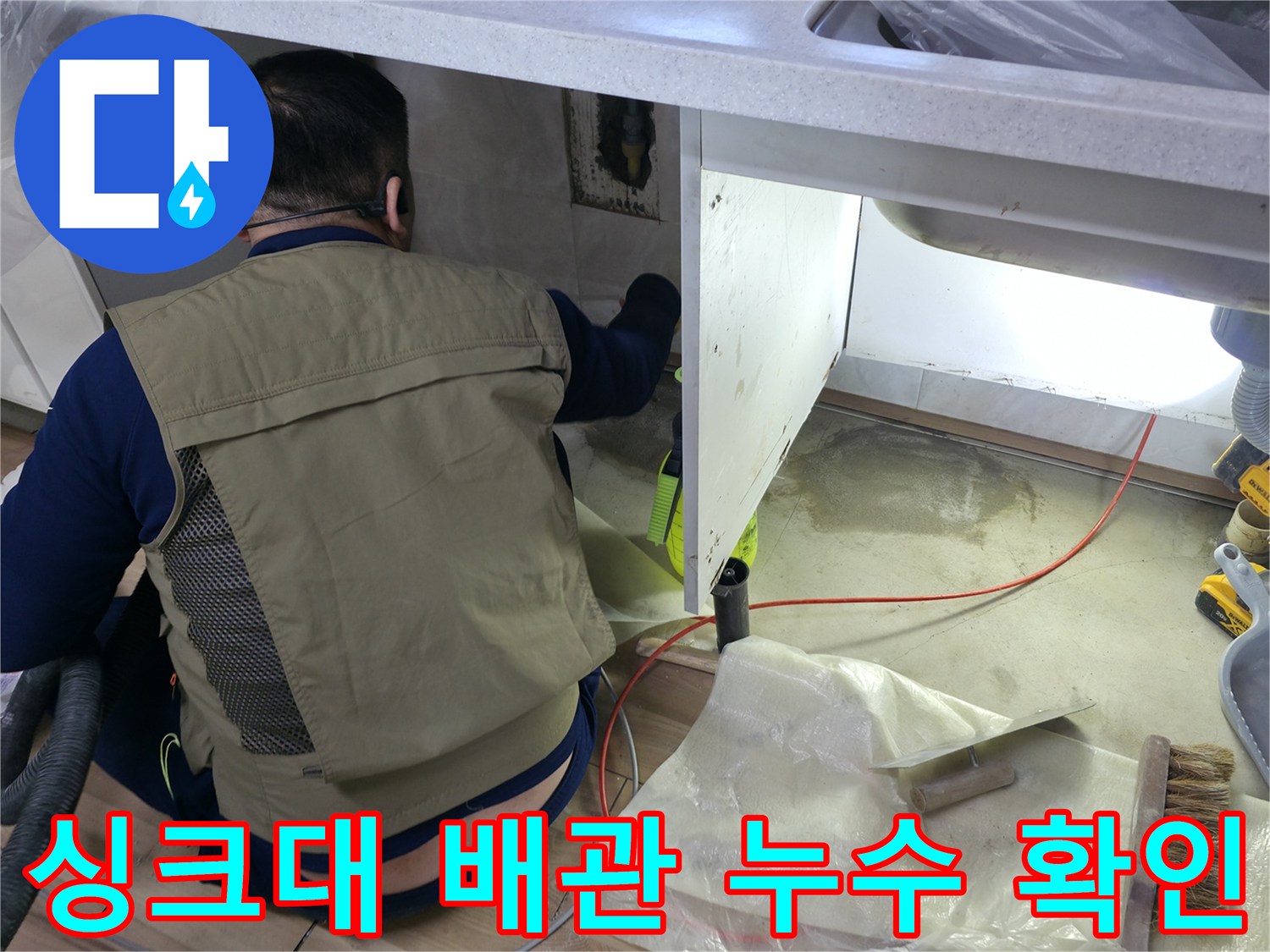 싱크대 하부장 아래쪽의 수도 배관을 점검하고 있는 장면입니다.