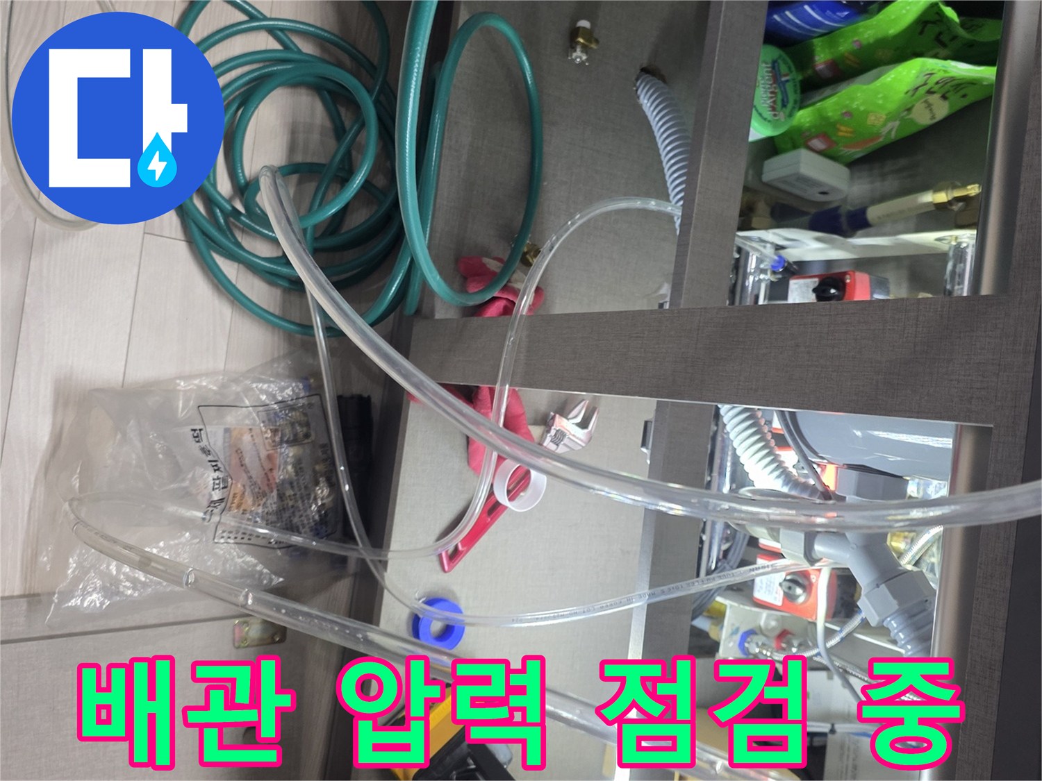 욕실 하부장 내-배관 공압 검사를 위해 설치된 압력 게이지와 호스
