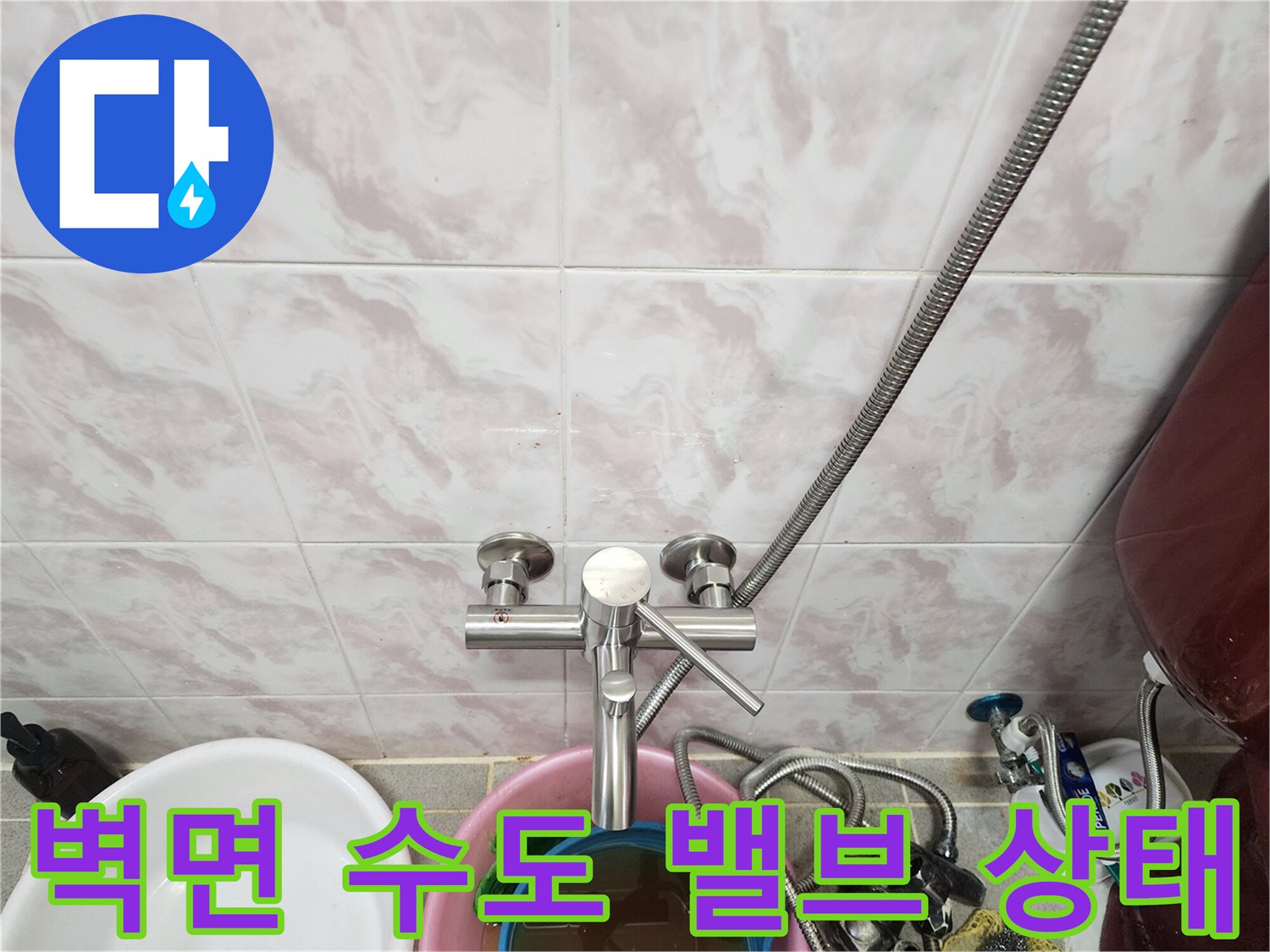 타일 벽면에 설치된 은색 수도 밸브와 연결된 금속 호스입니다.