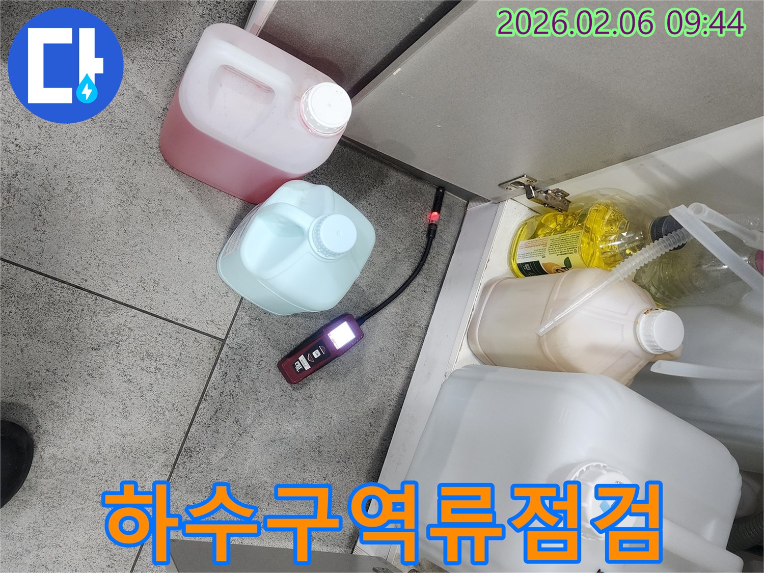 싱크대 하부장 아래에서 누수탐지 장비가 하수구 역류로 인한 누수 여부를 점검하고 있습니다
