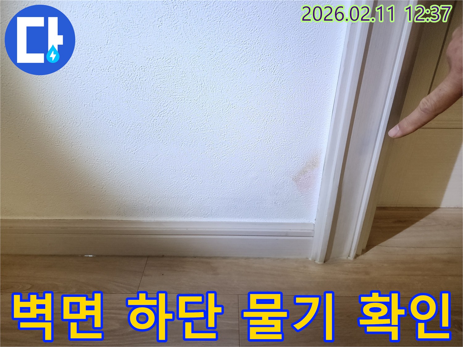 벽면 하단에 물기가 스며들어 벽지가 젖고 변색된 모습으로- 누수로 인한 피해가 진행 중임을 보여줍니다.