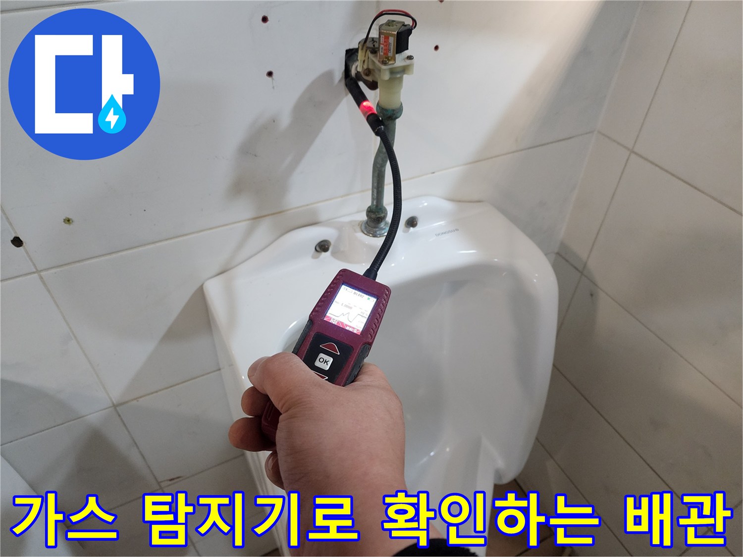 화장실 벽면 하단부에서 가스 탐지기를 사용하여 배관의 누수 지점을 추적하고 있습니다.