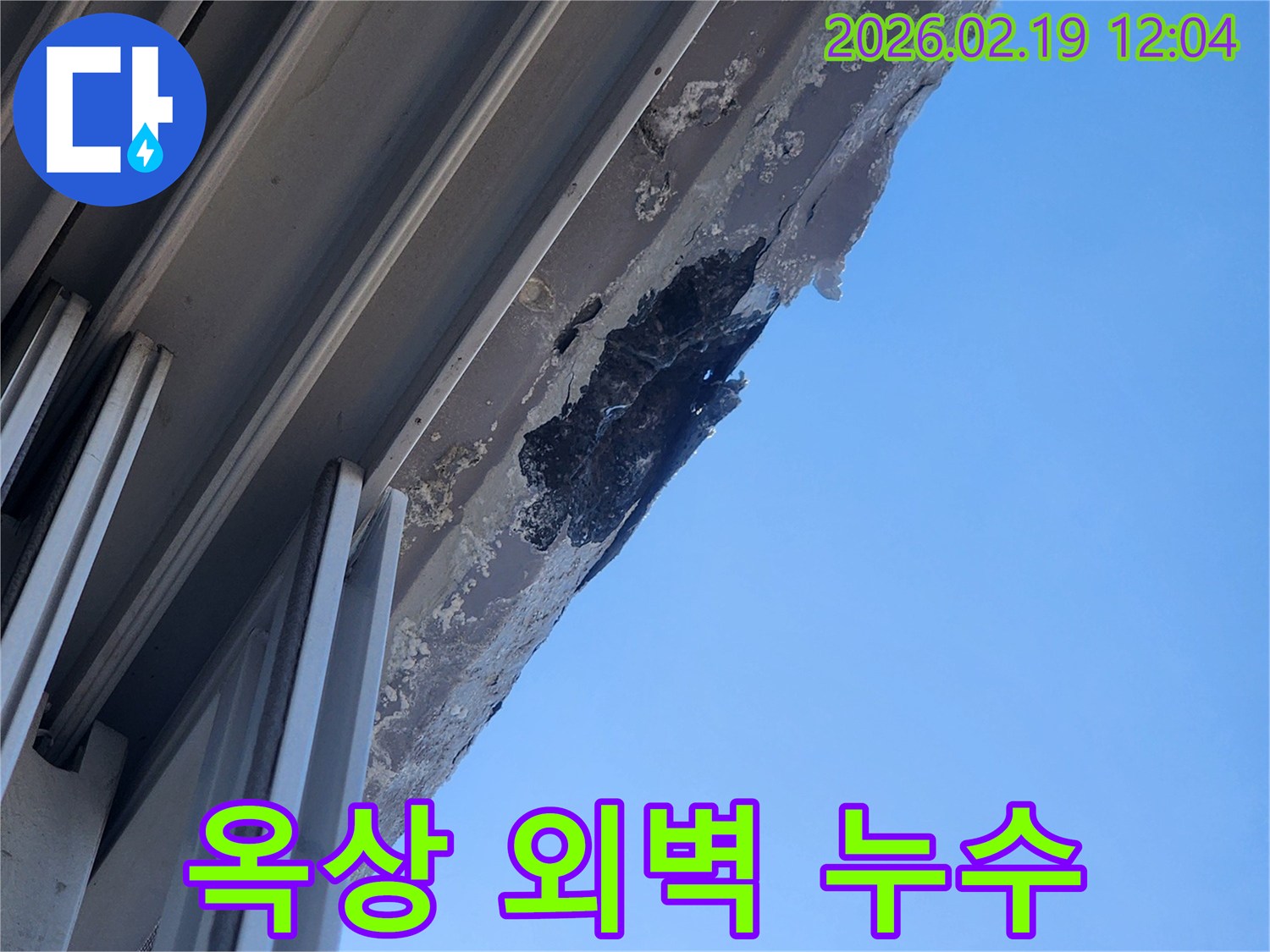 푸른 하늘 아래-건물 옥상과 맞닿은 외벽의-심각한 누수 손상과-마감재 박리 현장을 담은 사진