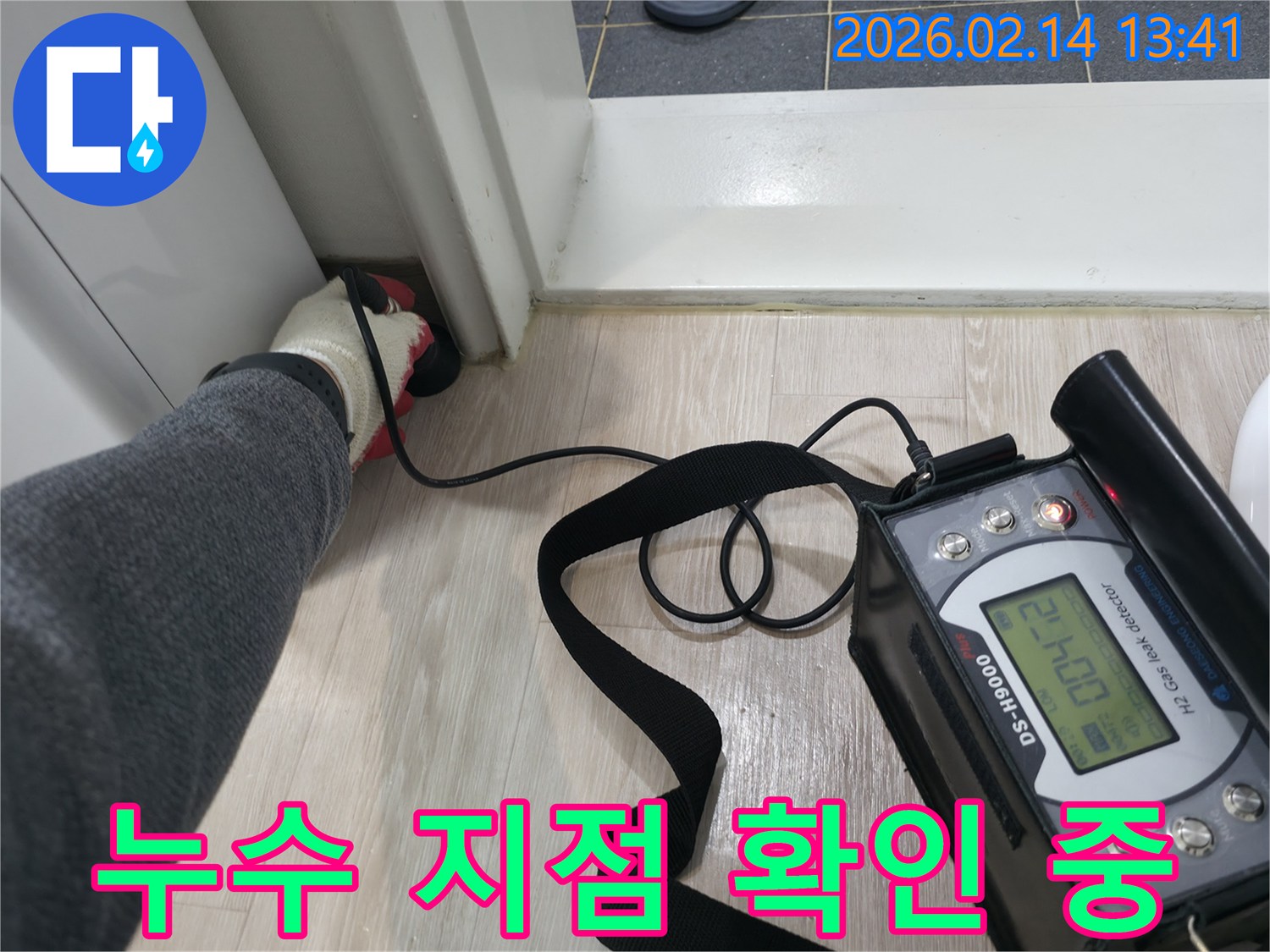 누수 탐지 엔지니어가-장갑을 착용하고-전문 탐지 장비의 센서를-바닥에 밀착시켜-누수 지점을 탐색하는 장면입니다.