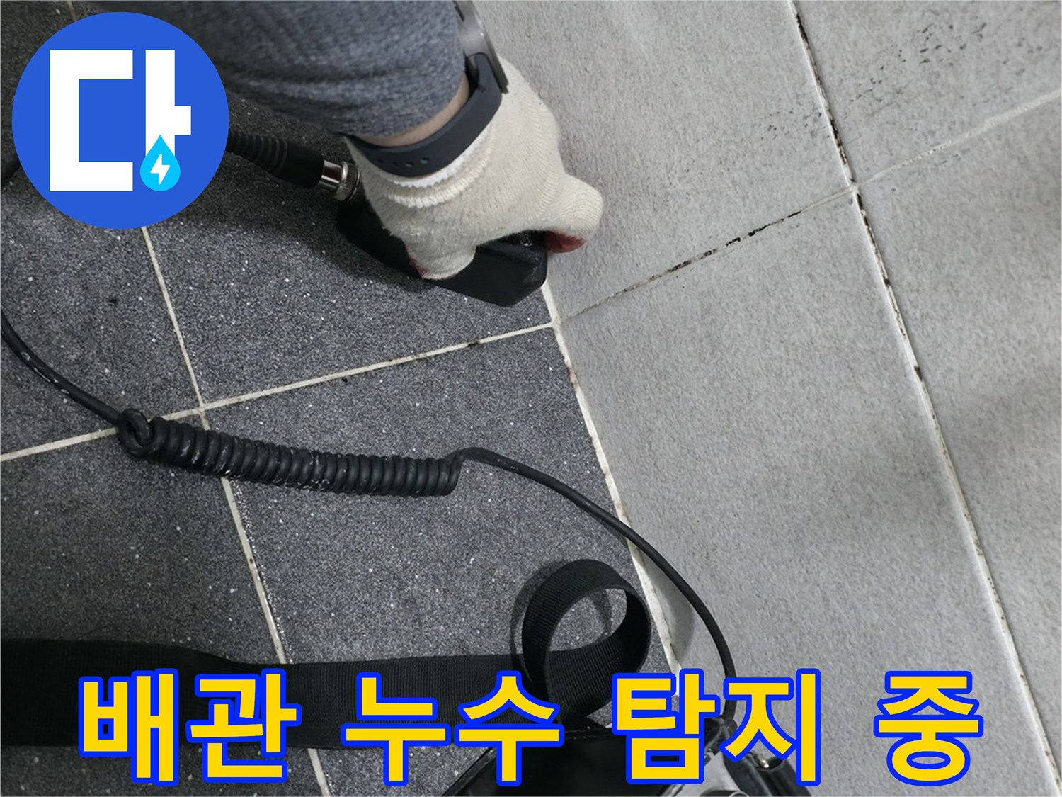 바닥 타일 근처에서 청음 장비를 사용하여 배관의 파손 여부를 진단하는 장면입니다.