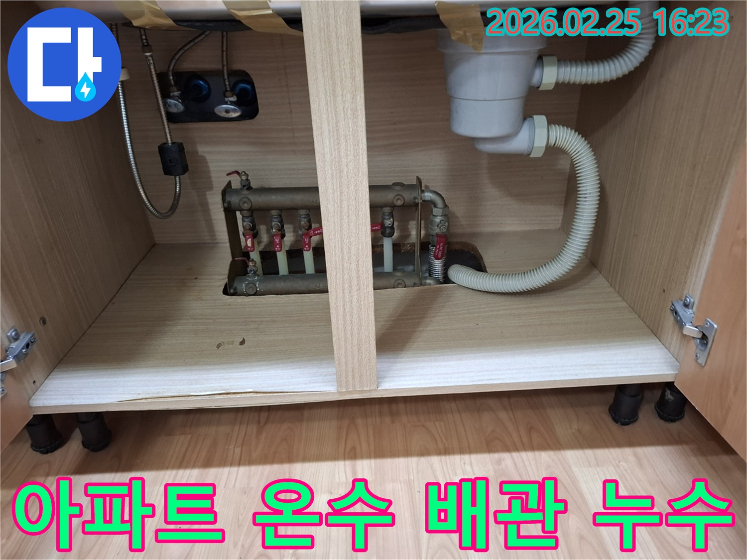 아파트 싱크대 하부장 내부에 설치된 온수 배관에서 물이 새는 현장 사진입니다