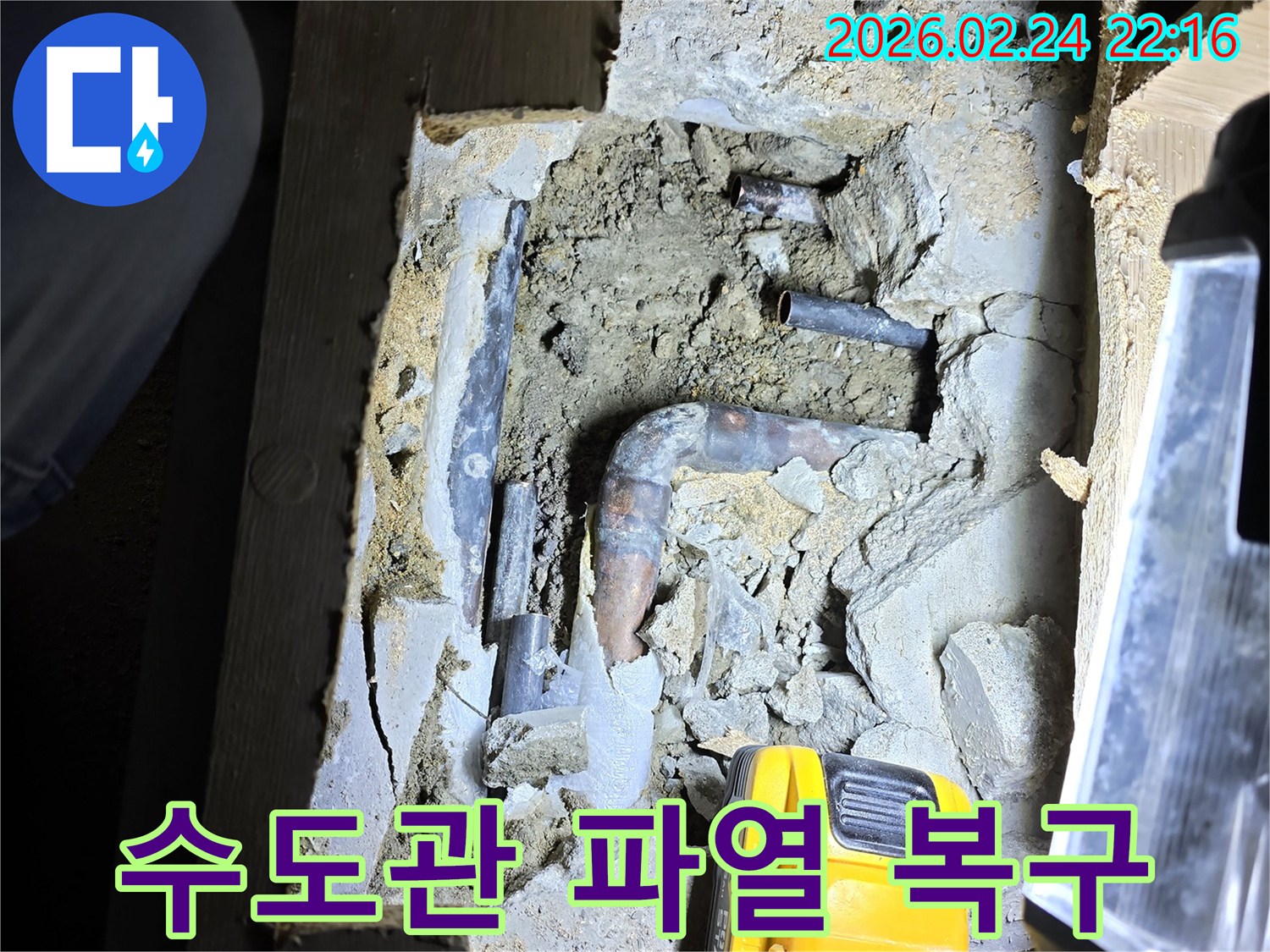 어두운 바닥 아래-손전등으로 비추며-숨겨진 수도관의-파열 지점을-정확히 확인하고-복구 작업을-준비하는 모습입니다.