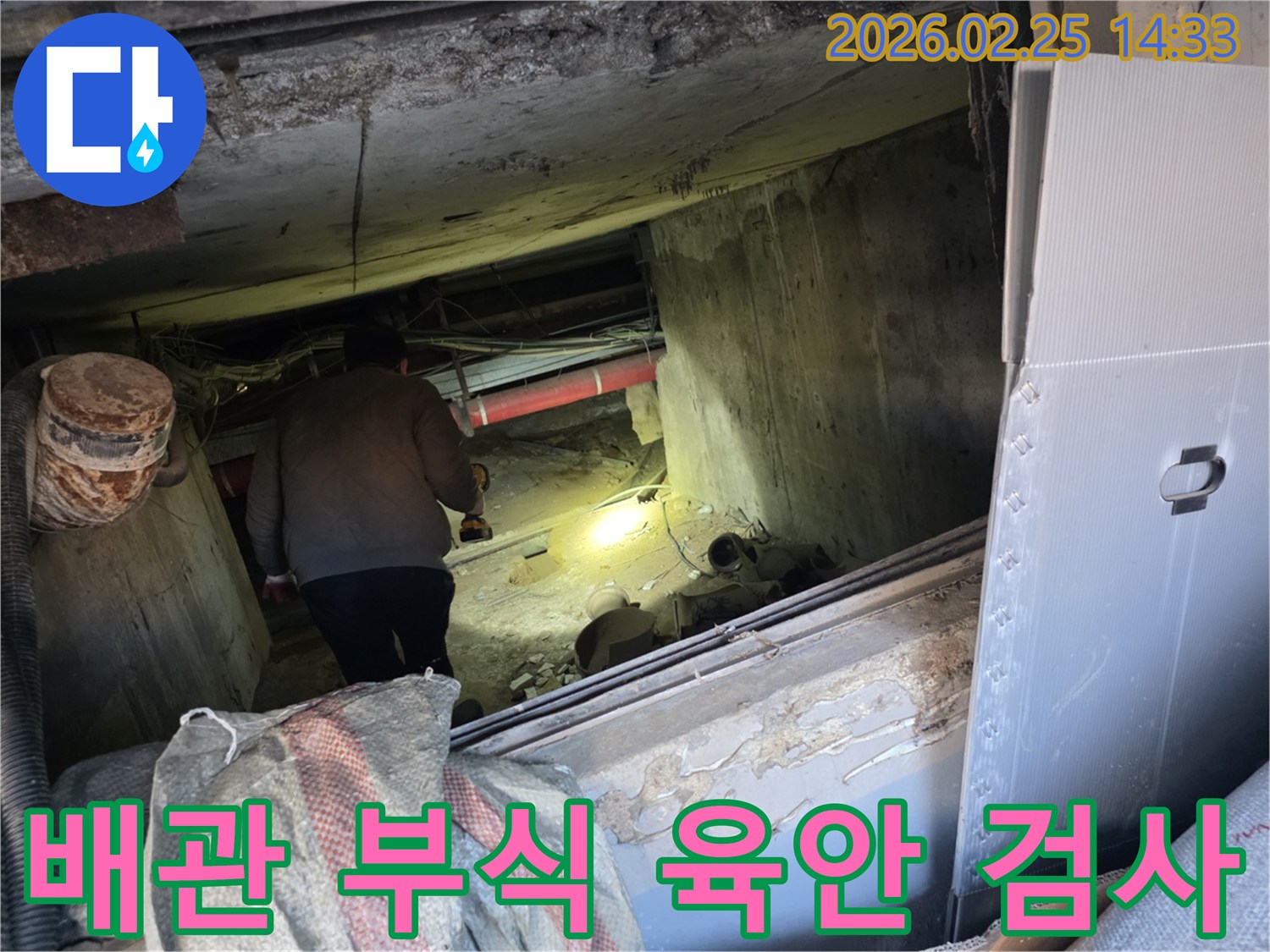 누수 전문 엔지니어가-어둡고 좁은 공간에서-손전등을 비춰가며-배관의 부식 여부를-육안으로 꼼꼼히-검사하는 모습입니다.