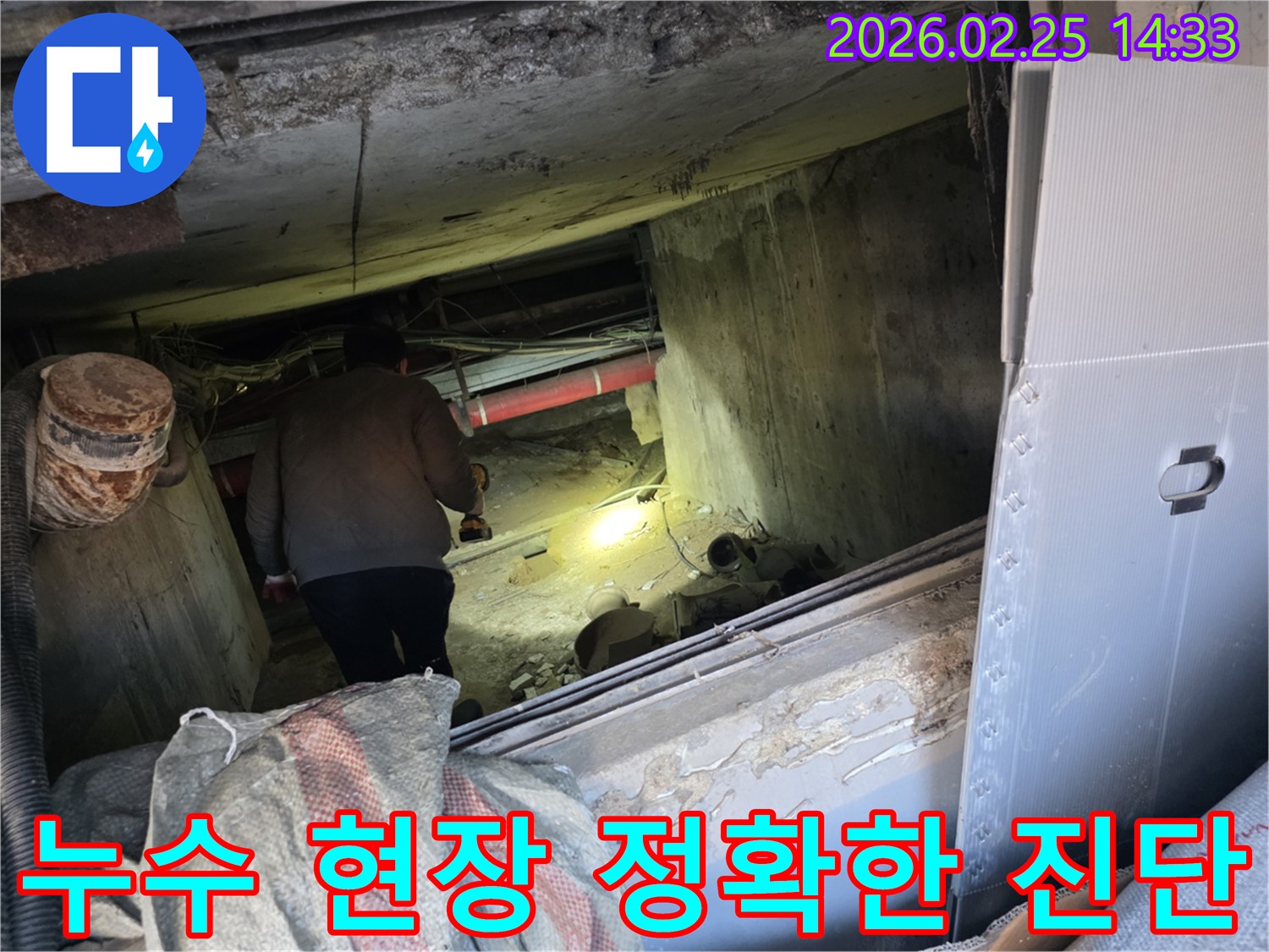 누수 전문 엔지니어가-어둡고 좁은 현장에서-손전등을 비춰가며-누수의 정확한 원인을-진단하기 위해-배관을 면밀히 살피는 모습입니다.