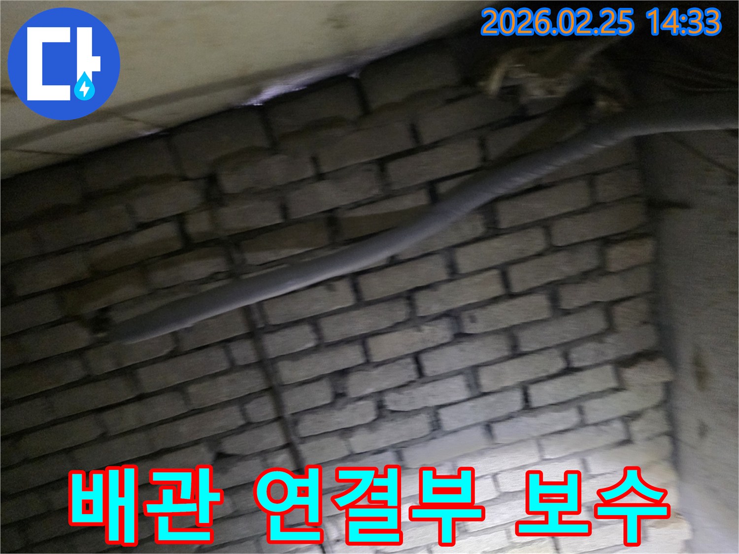 어두운 벽돌 벽면을 배경으로-단열된 배관의 연결부에서-누수 보수 작업을 위해-정밀하게 검사되는 현장 모습입니다.