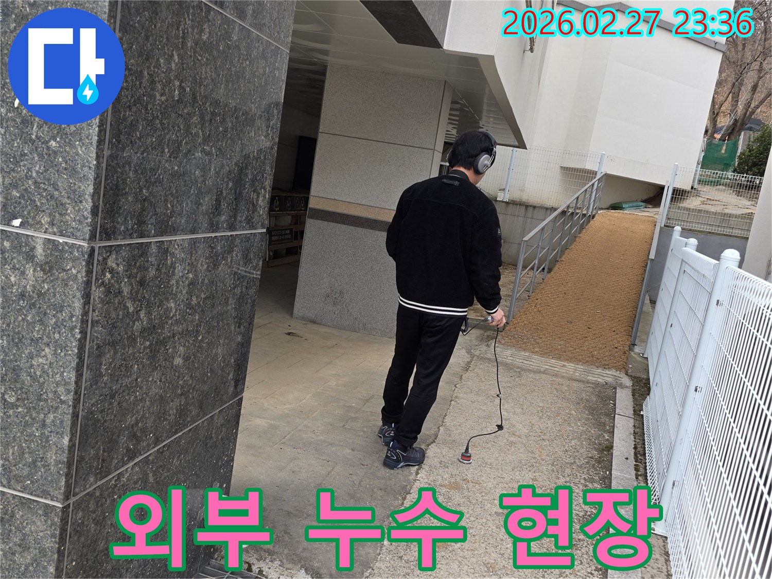 누수 엔지니어가-청음식 탐지기로-건물 외부에서-누수 지점을 탐지하고-현장 상황을 보고하는 모습