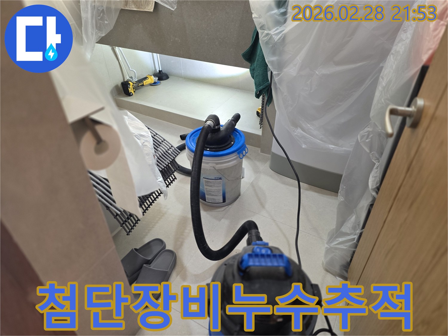 이 이미지는 누수 현장에서-주변을 비닐로 보양하고-습식 청소기와 조명 장비를 사용하여-첨단 기술로 누수 흔적을 정밀하게 추적하는 모습을 보여줍니다.