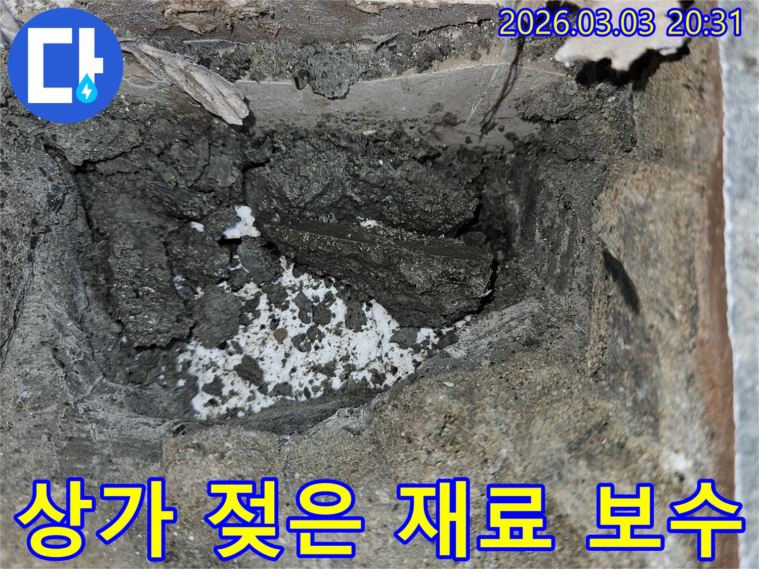 상가 벽면 누수로 인해 손상된 부위를 철거하고 있습니다-내부의 젖은 시멘트와 부서진 잔해가 보입니다.