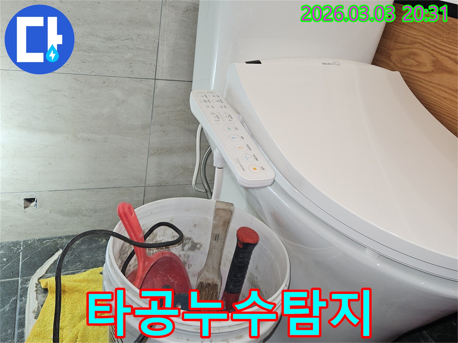 이 이미지는-화장실 바닥 타일에 작은 타공을 하고-누수 탐지 작업을 시작하기 위해-공구들을 준비한 현장 모습을 보여줍니다.