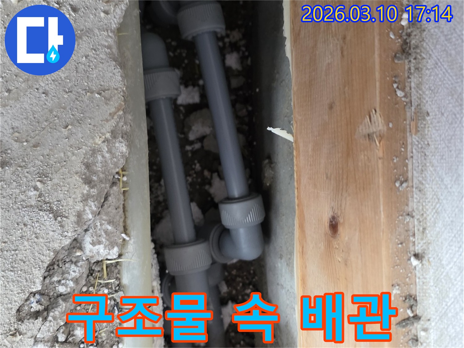 주택 바닥의 콘크리트 및 목재 구조물 사이에-새로운 배관을 안전하게 설치하여-누수 문제를 해결하는 공사 현장 이미지입니다.