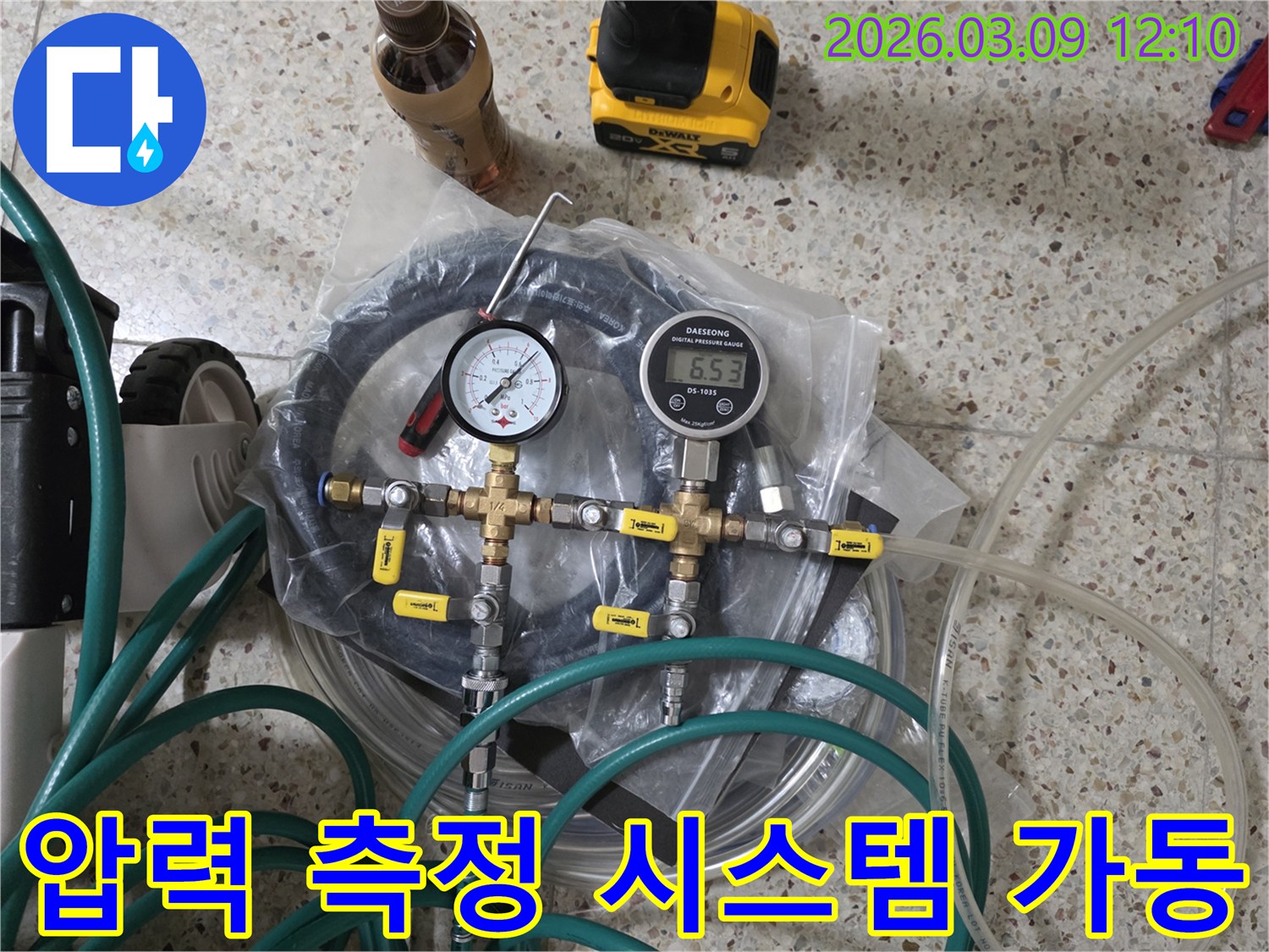 누수 탐지를 위한 배관 압력 측정 시스템의-핵심 부품인 게이지와-연결 호스-밸브들이 바닥에 놓여 있습니다.