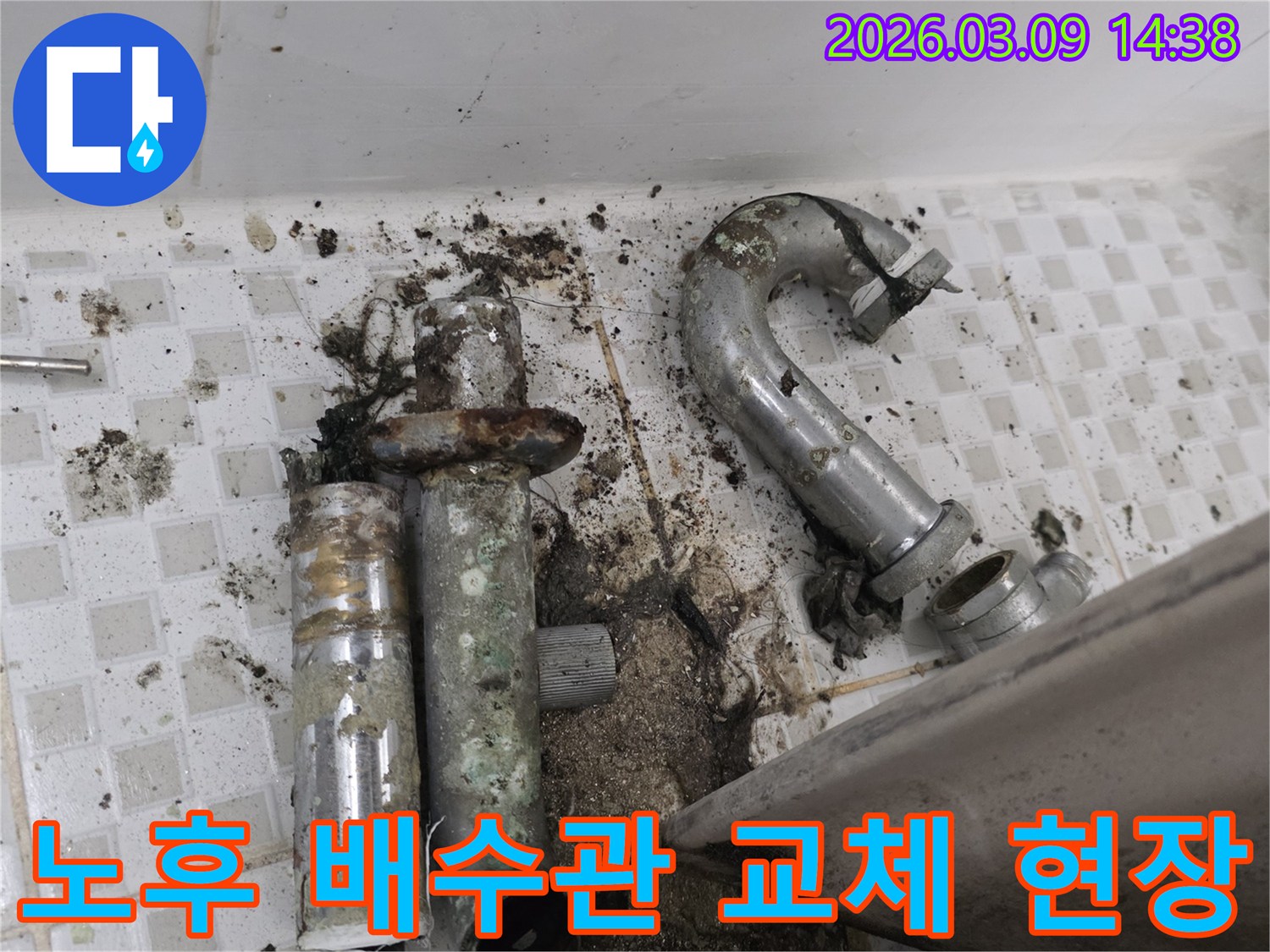 이 사진은 노후화로 인해 파손된 욕실 배수관과-그로 인해 오염된 주변 바닥을 보여줍니다-새 배관으로 교체하기 전의 모습입니다