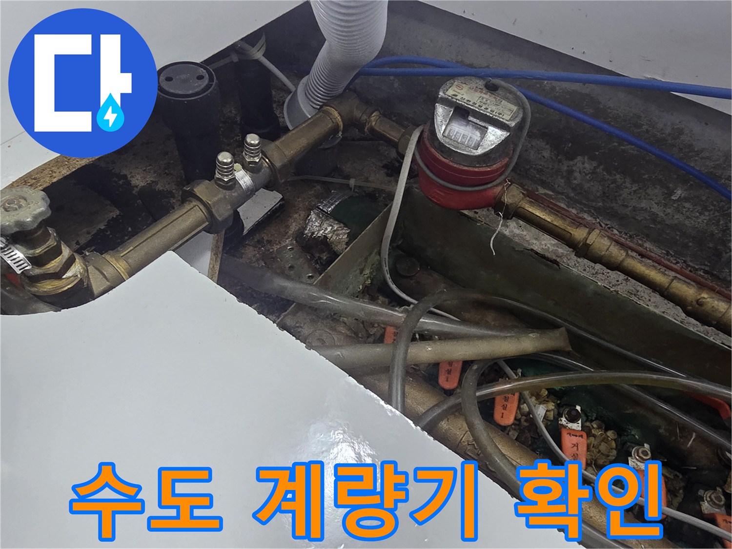 붉은색 수도 계량기와 연결된 금속 배관의 근접 촬영 사진입니다.