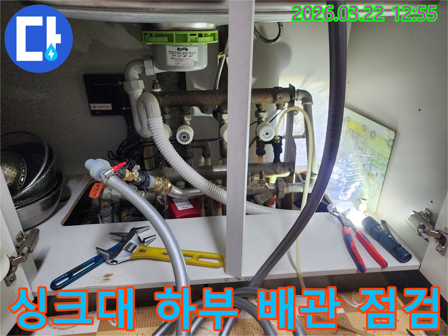 싱크대 하부의 복잡한 배관들을-누수 탐지 장비와 함께-꼼꼼하게 점검하는-전문가의 모습입니다.