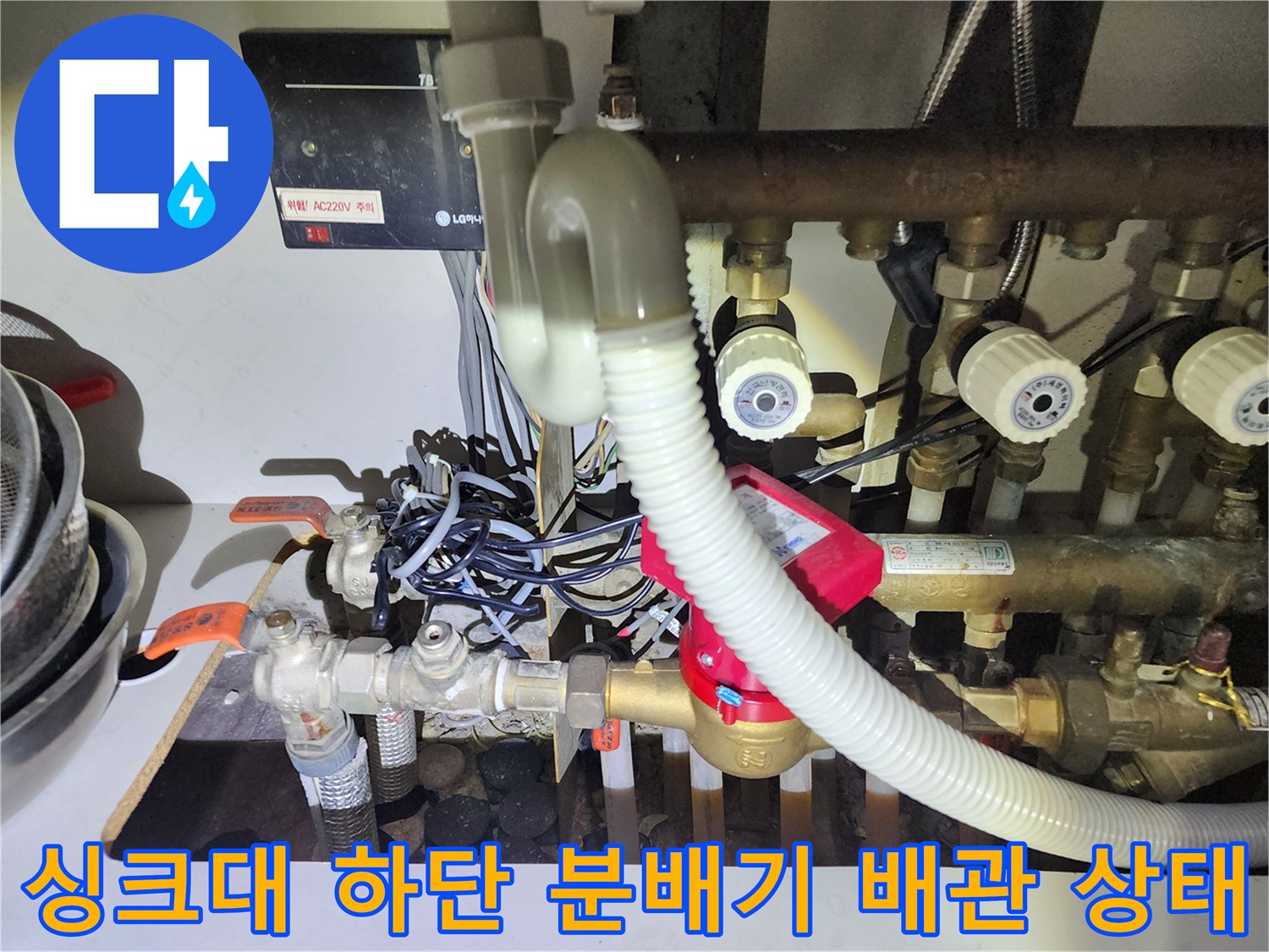 용산구 현장의 싱크대 아래 복잡하게 연결된 난방 분배기 및 배관 모습입니다.