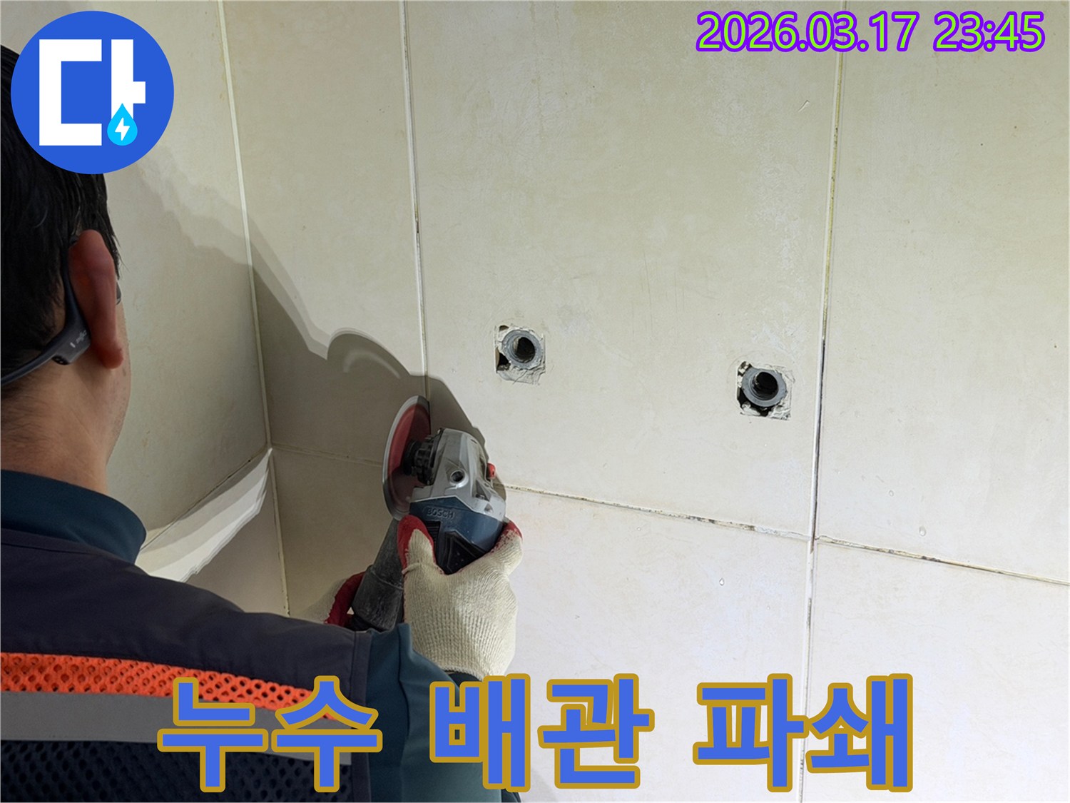 누수된 배관을-노출시키기 위해-전문가가-타일 벽면을-그라인더로-조심스럽게-파쇄하고-있습니다