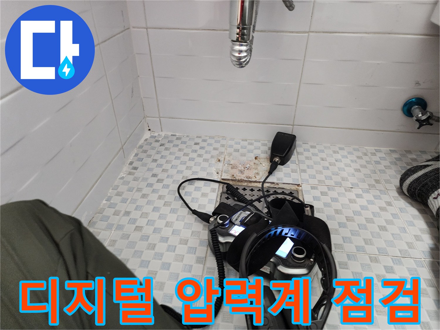 바닥 타일 위에 배치된 디지털 압력계와 탐지용 헤드셋-배관 내 공압 검사를 진행 중인 모습입니다.