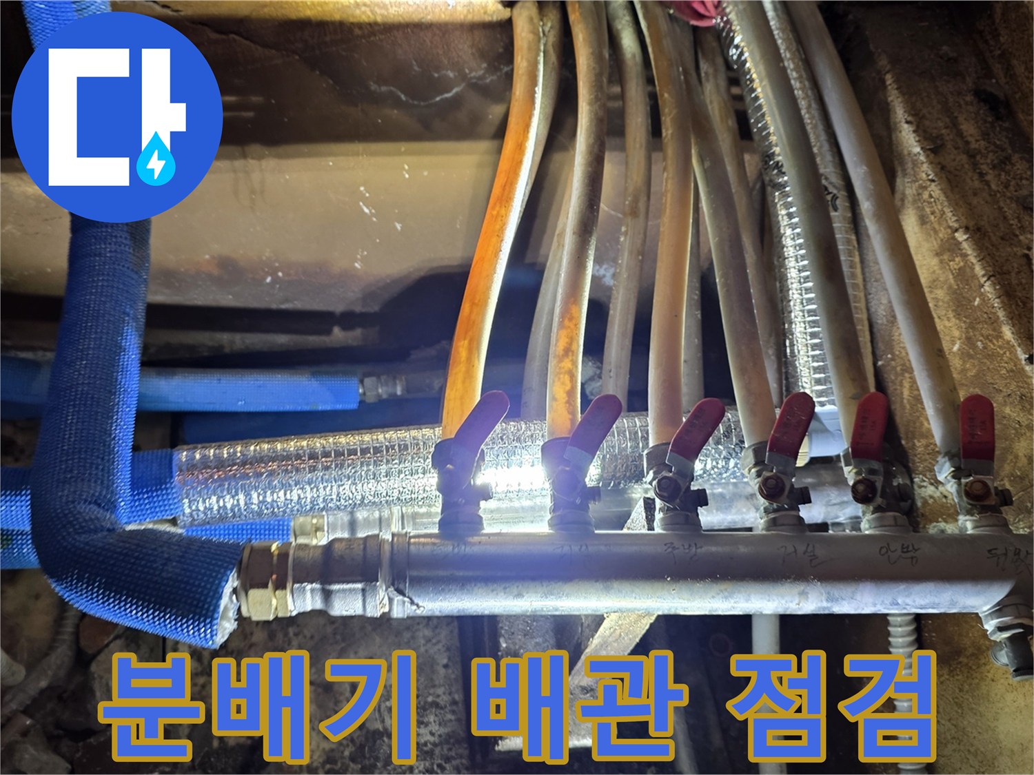 금속 분배기와 파란색 보온재가 씌워진 난방 배관의 모습