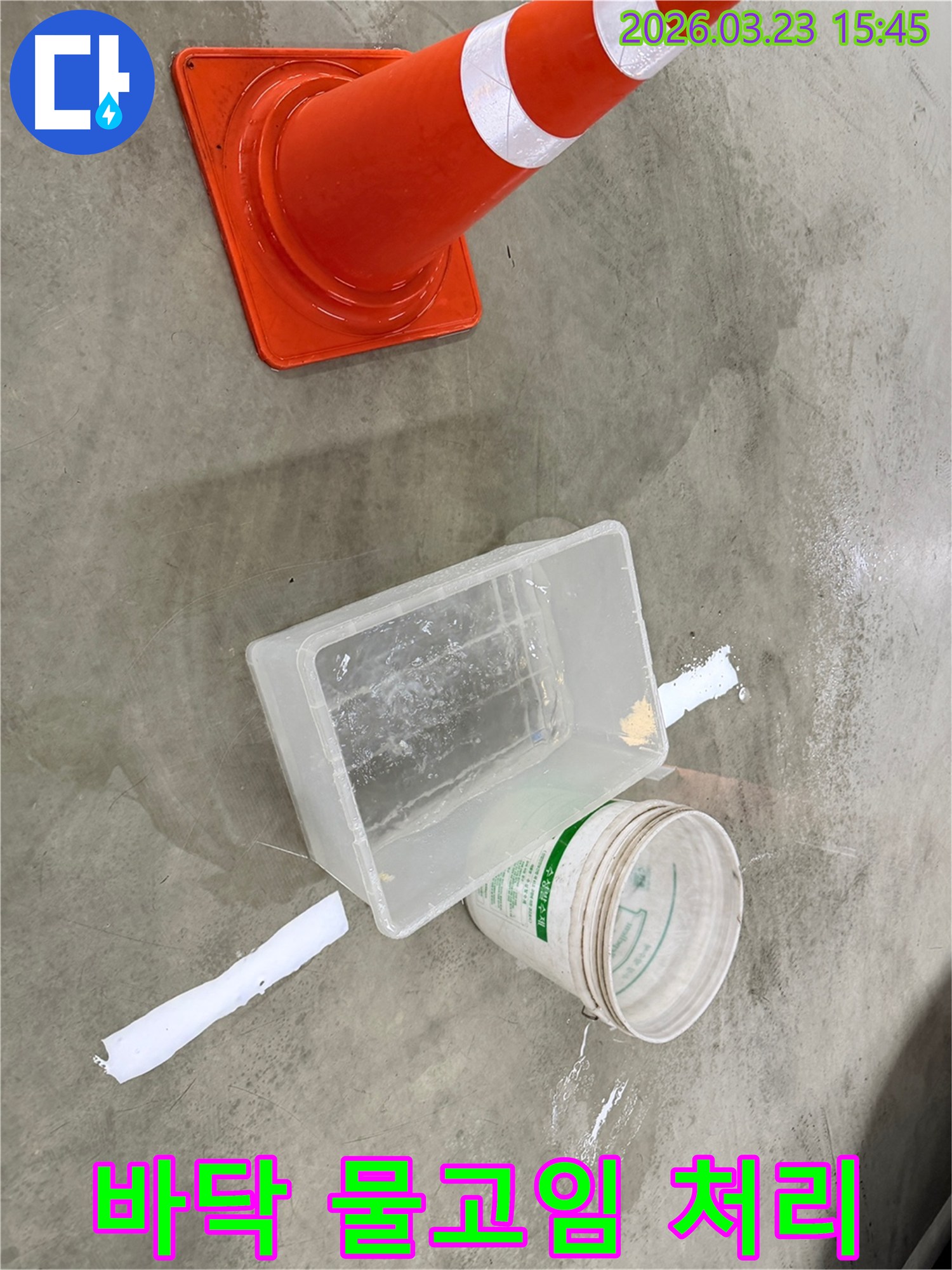 바닥에 물기가 흥건한 누수 현장에서-안전 콘과 물받이 용기를 사용하여 상황을 관리하고 있습니다.