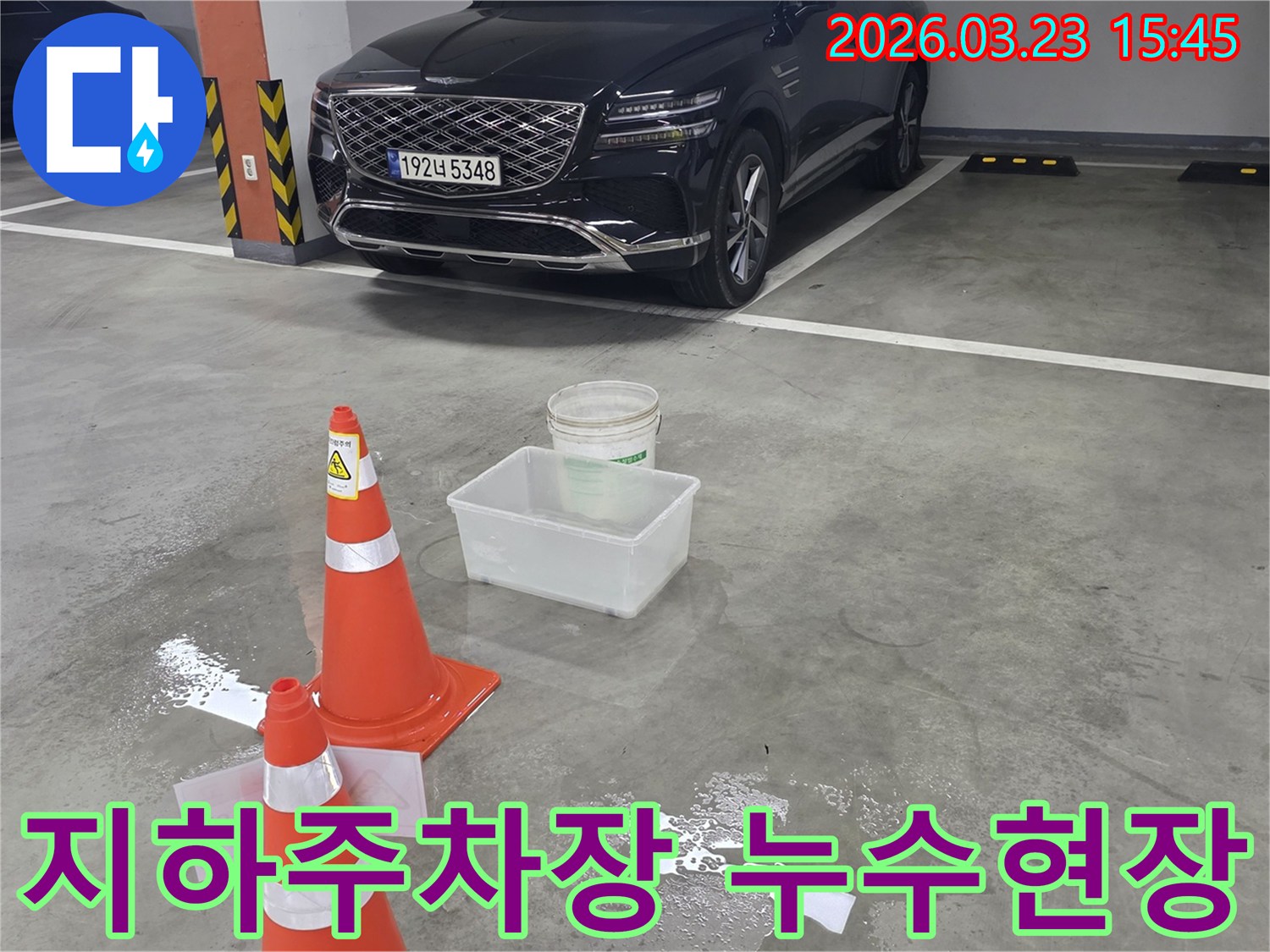 지하주차장 바닥에 물이 고여-안전 콘과 물받이가 설치된-누수 현장을 보여주는 이미지입니다.