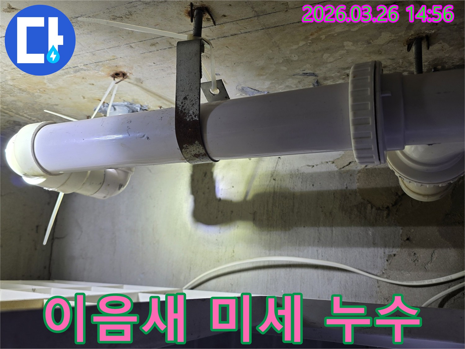 콘크리트 천장에 설치된-하얀색 배관의 나사식 이음새와-녹슨 금속 지지대 주변을-엔지니어가 손전등으로 면밀히 살피는 모습