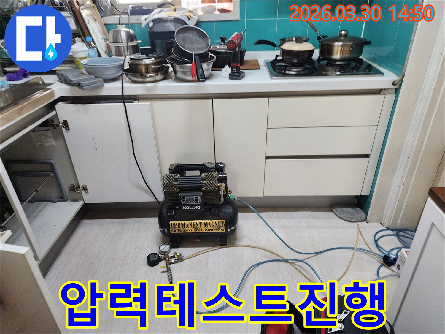 주방 하부장 아래에 설치된-공압 장비가-수도 배관에 압력을 가하여-누수 여부를 정밀하게 테스트하고 있습니다.