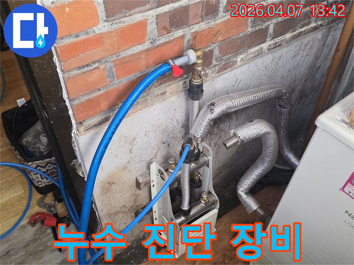 벽돌 벽 옆에-누수 탐지 장비가-설치되어 있으며-파란색 호스가-수도 배관에 연결되어-정밀 진단을 준비 중입니다.
