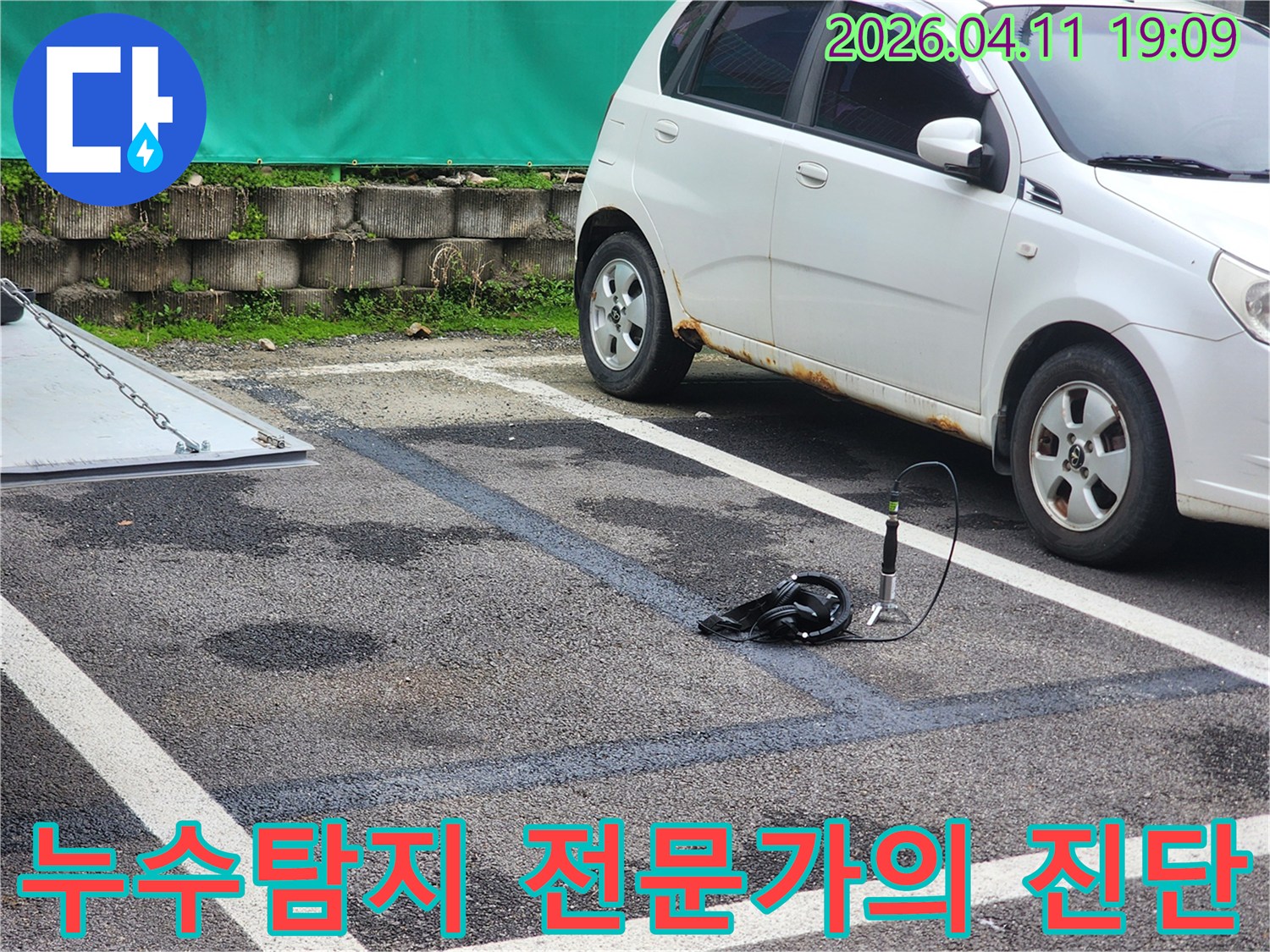 주차장 바닥에 물기가 보이는 곳에서-누수 지점을 찾기 위해-청음식 탐지 장비를 설치하여-전문가가 진단 중인 모습입니다.